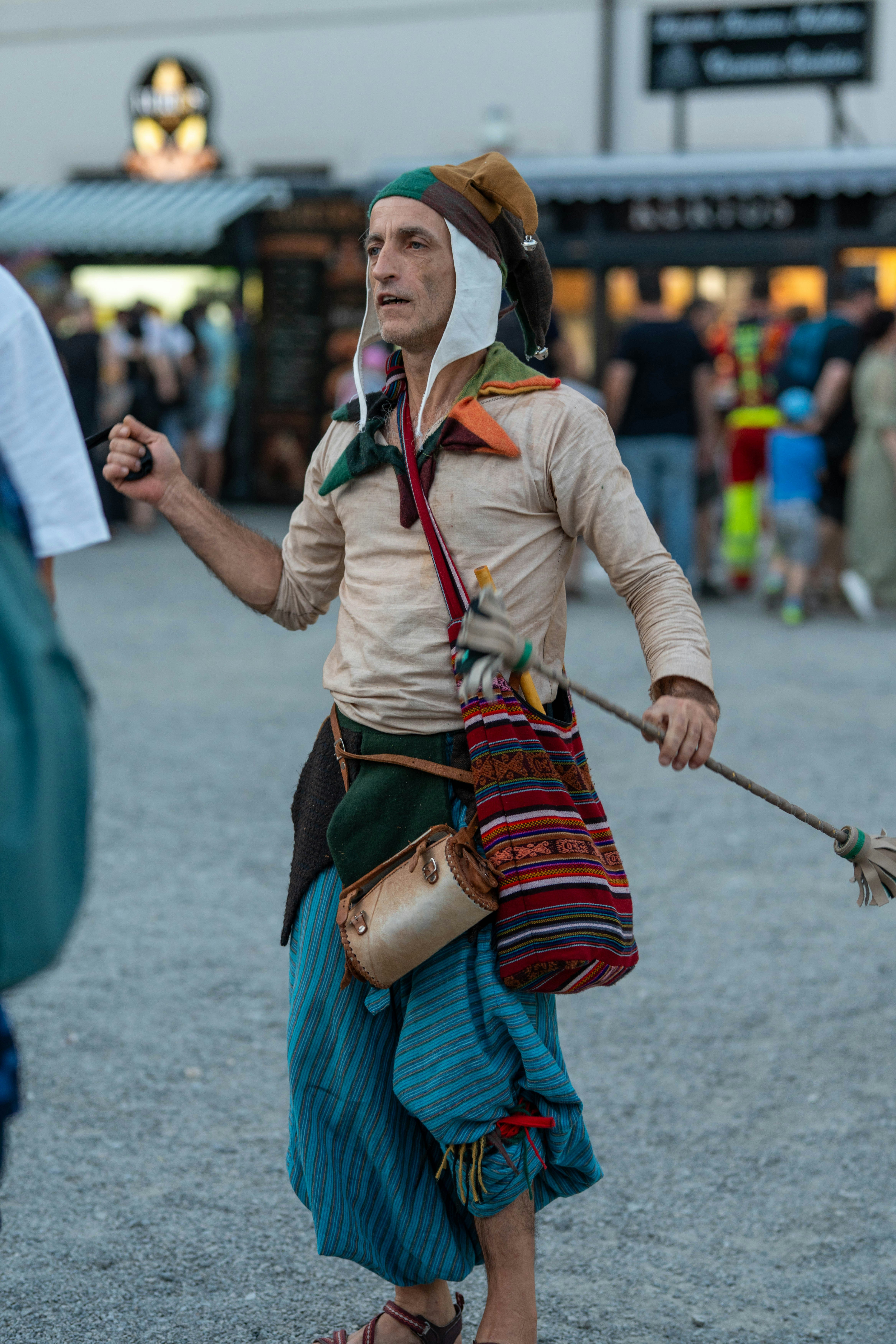 Jester in colorful costume holding a broom outdoors.