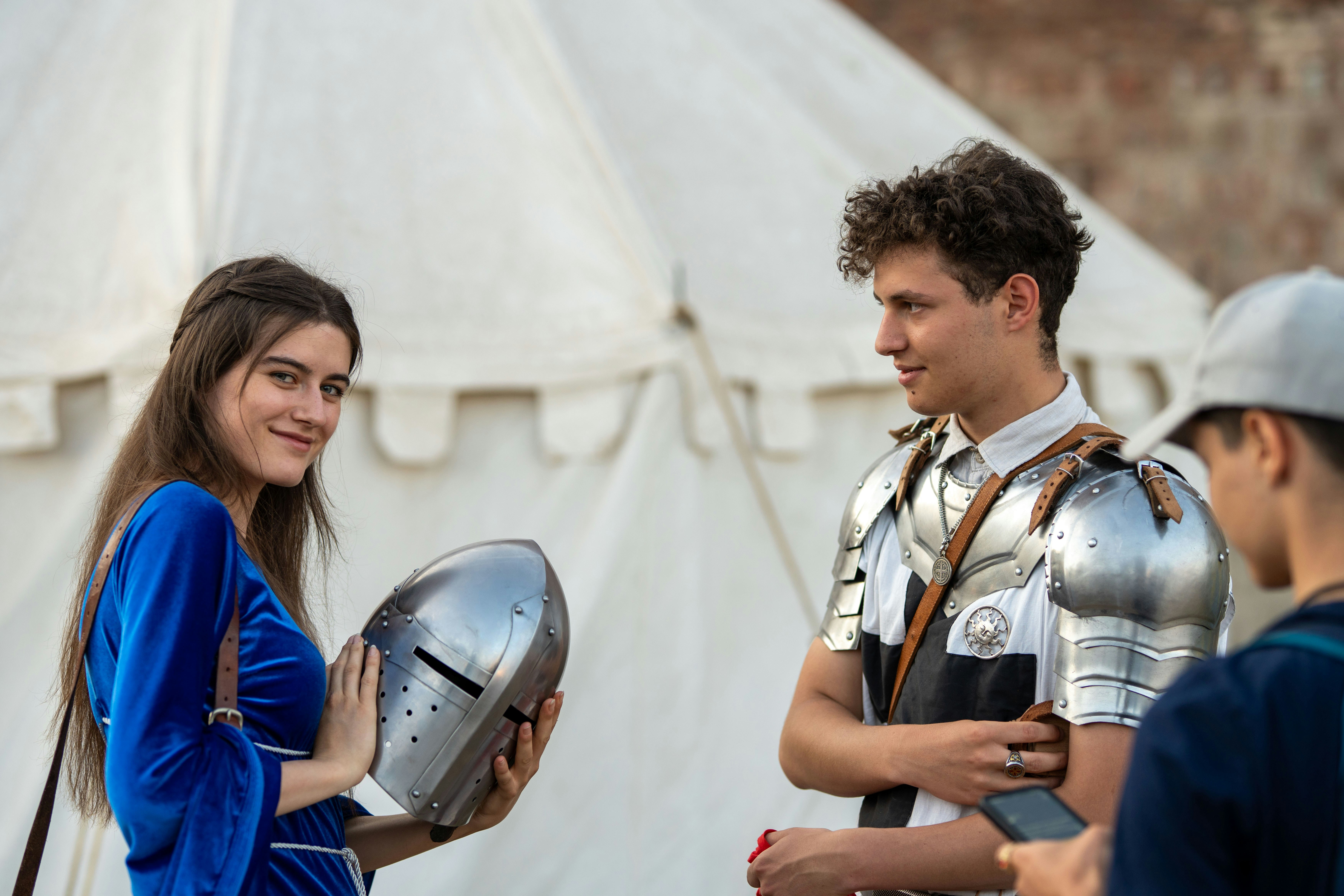 Woman in blue dress holds knight's helmet, man in armor.