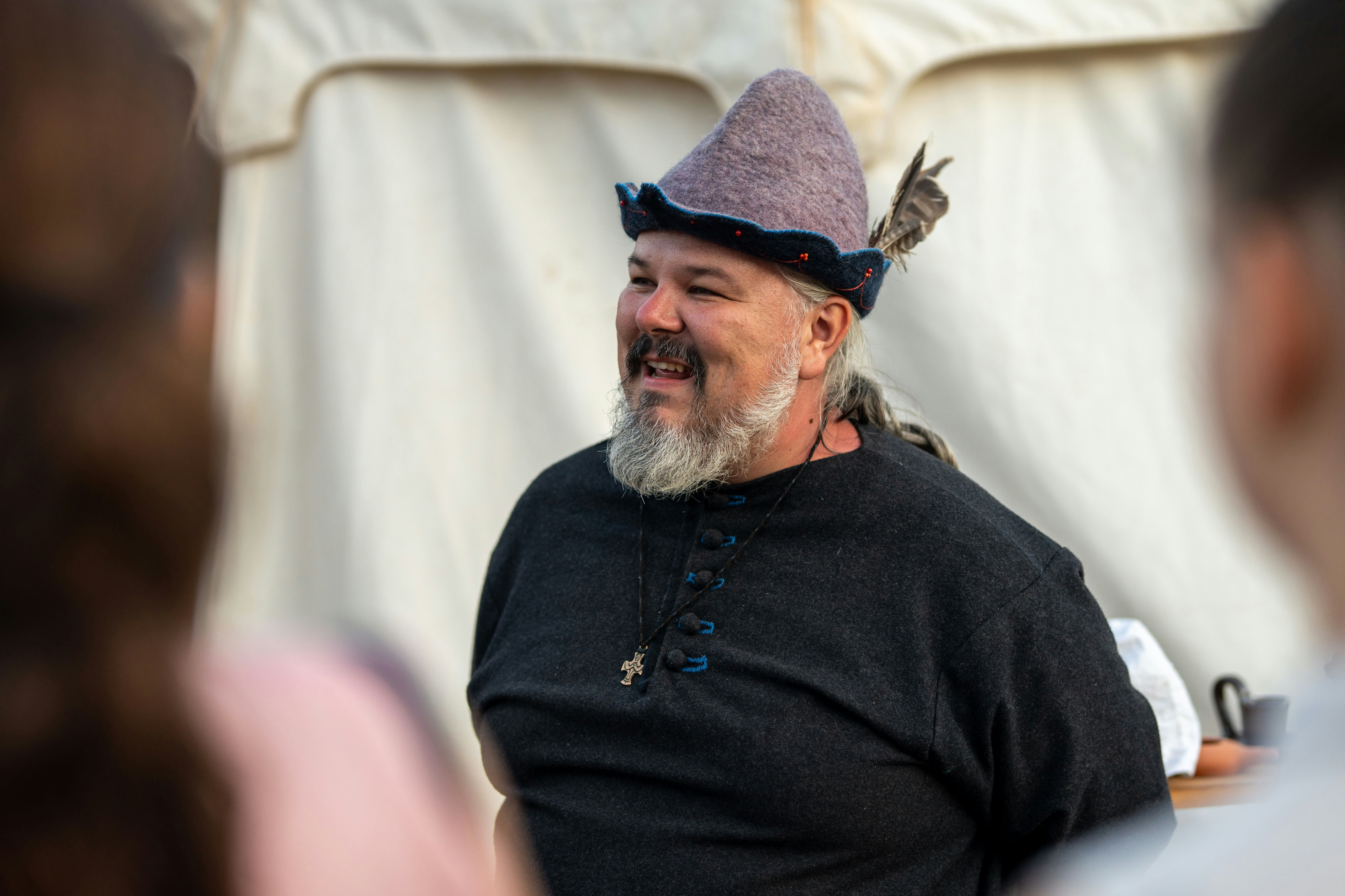 A bearded man in a feathered hat smiles.