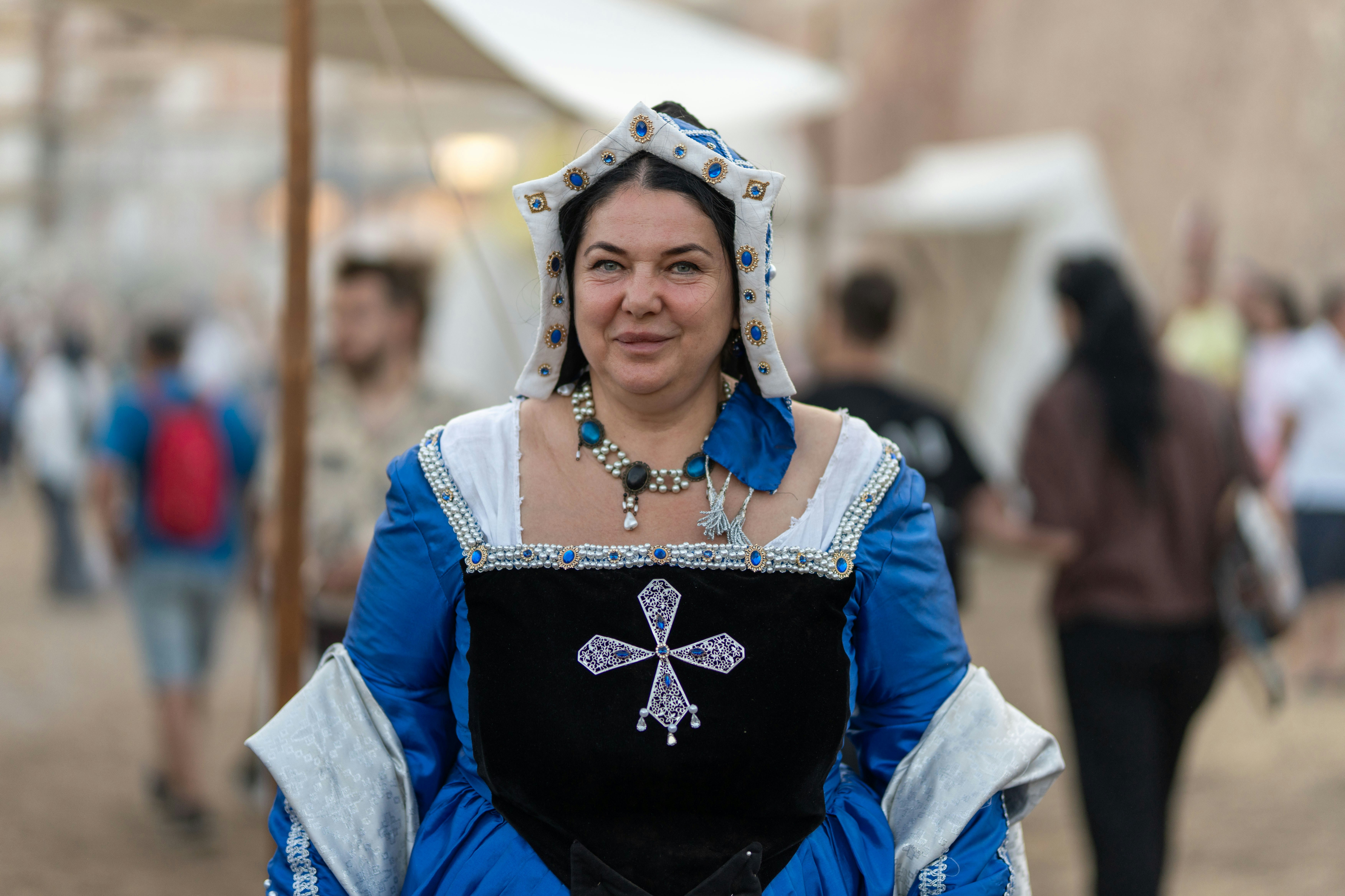 Donna sorridente con un abito medievale blu ornato e un copricapo.