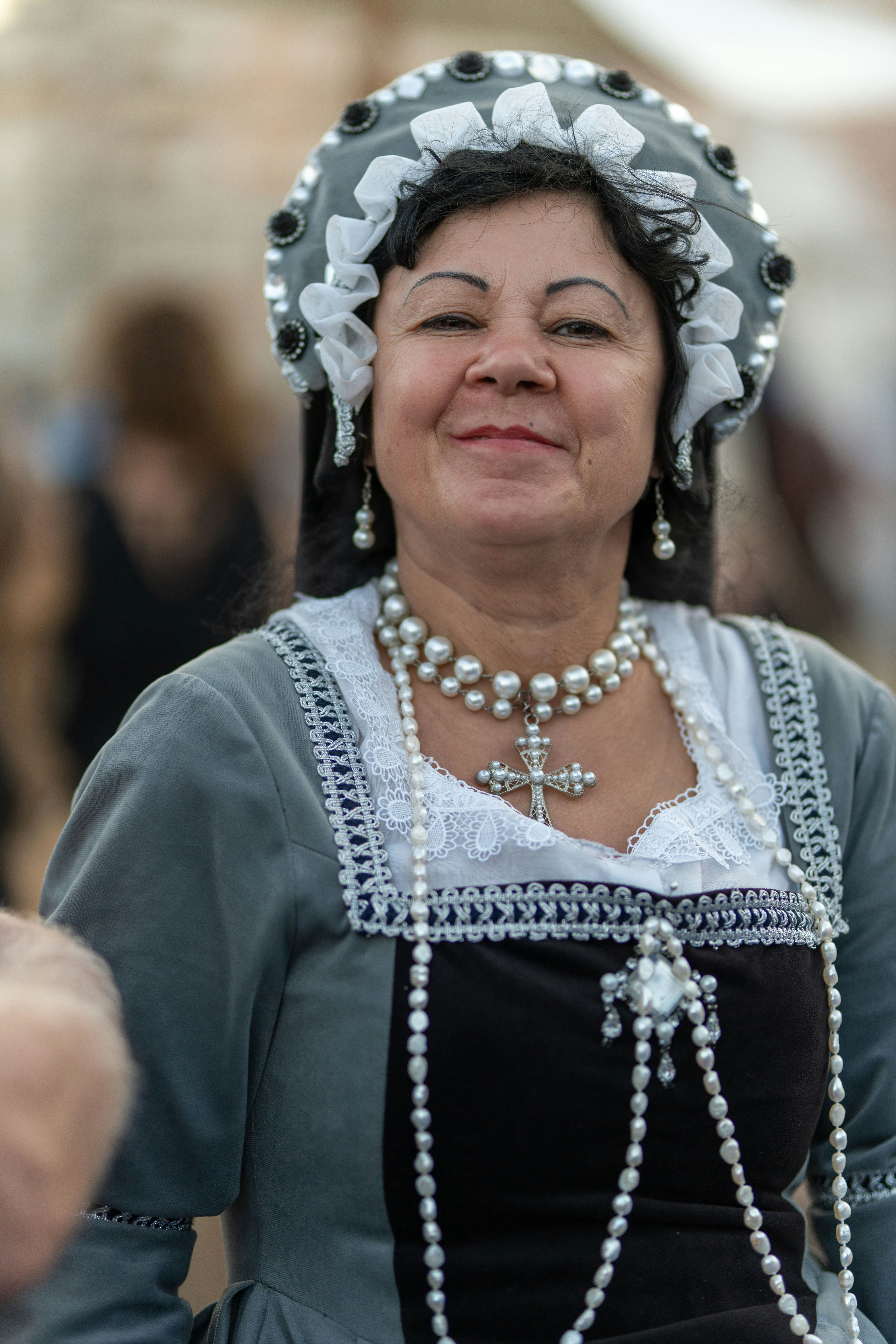 A smiling woman in historical attire with pearl jewelry.