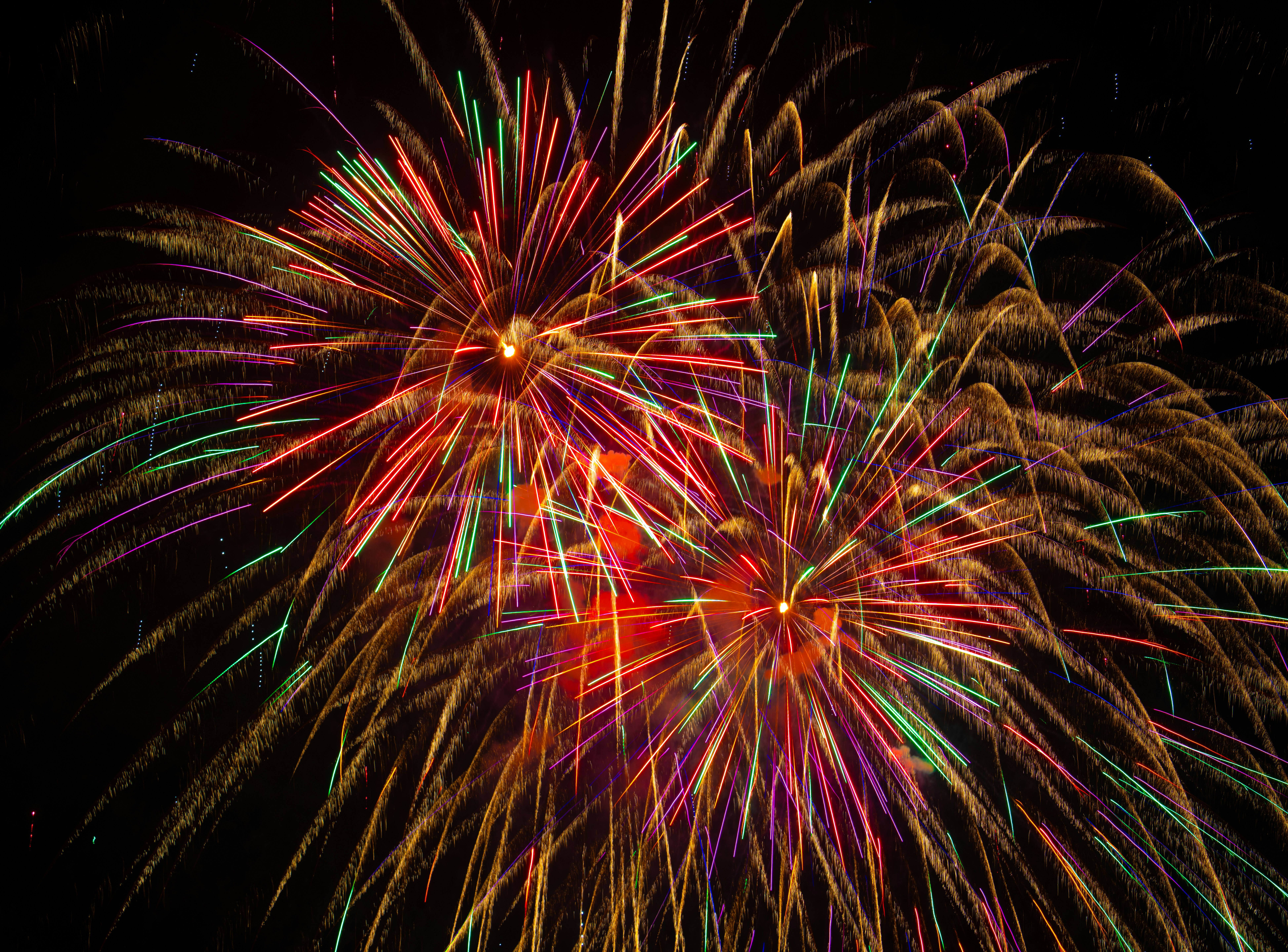 Colorful fireworks explode in the dark night sky.
