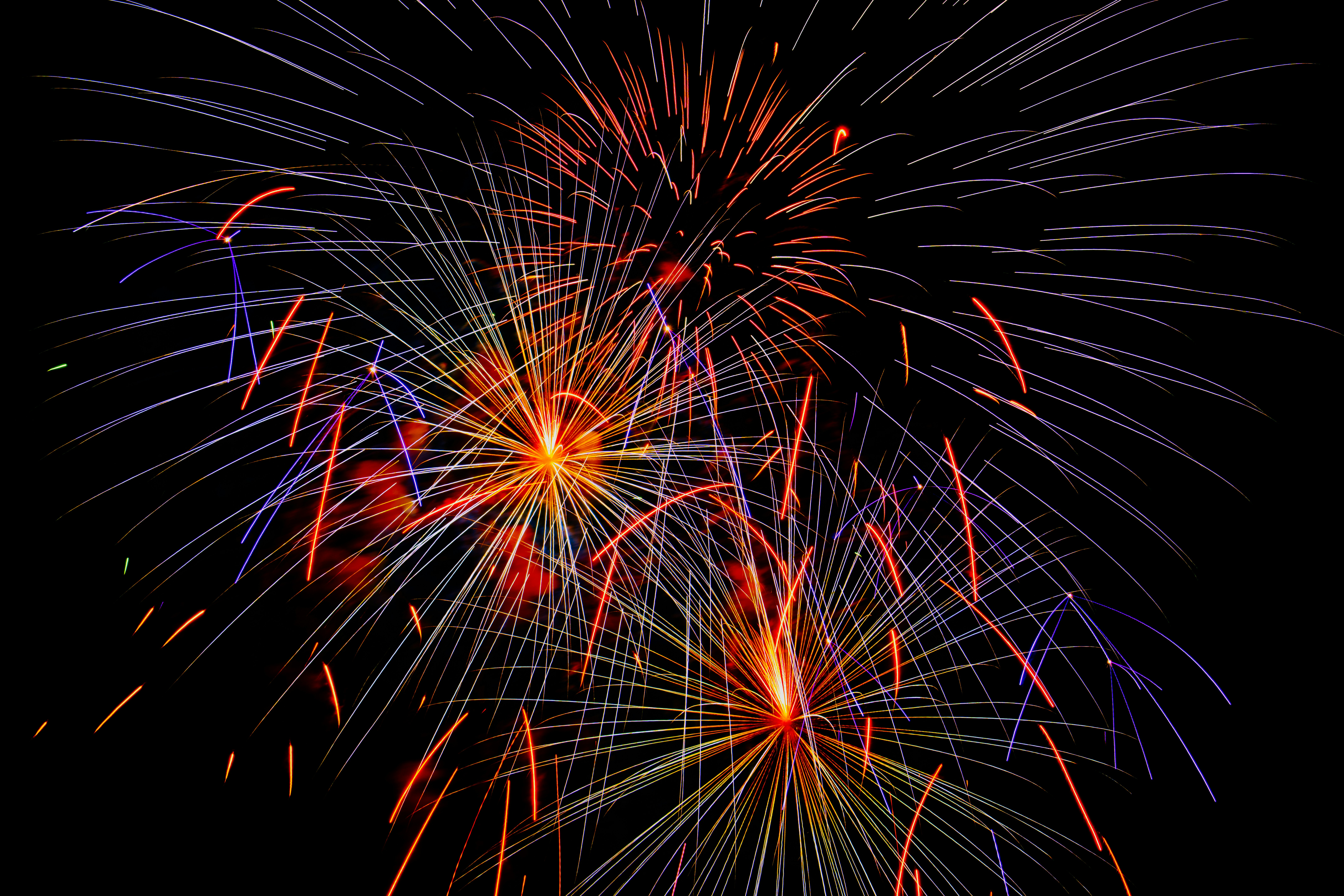 Bright fireworks burst across a dark night sky.