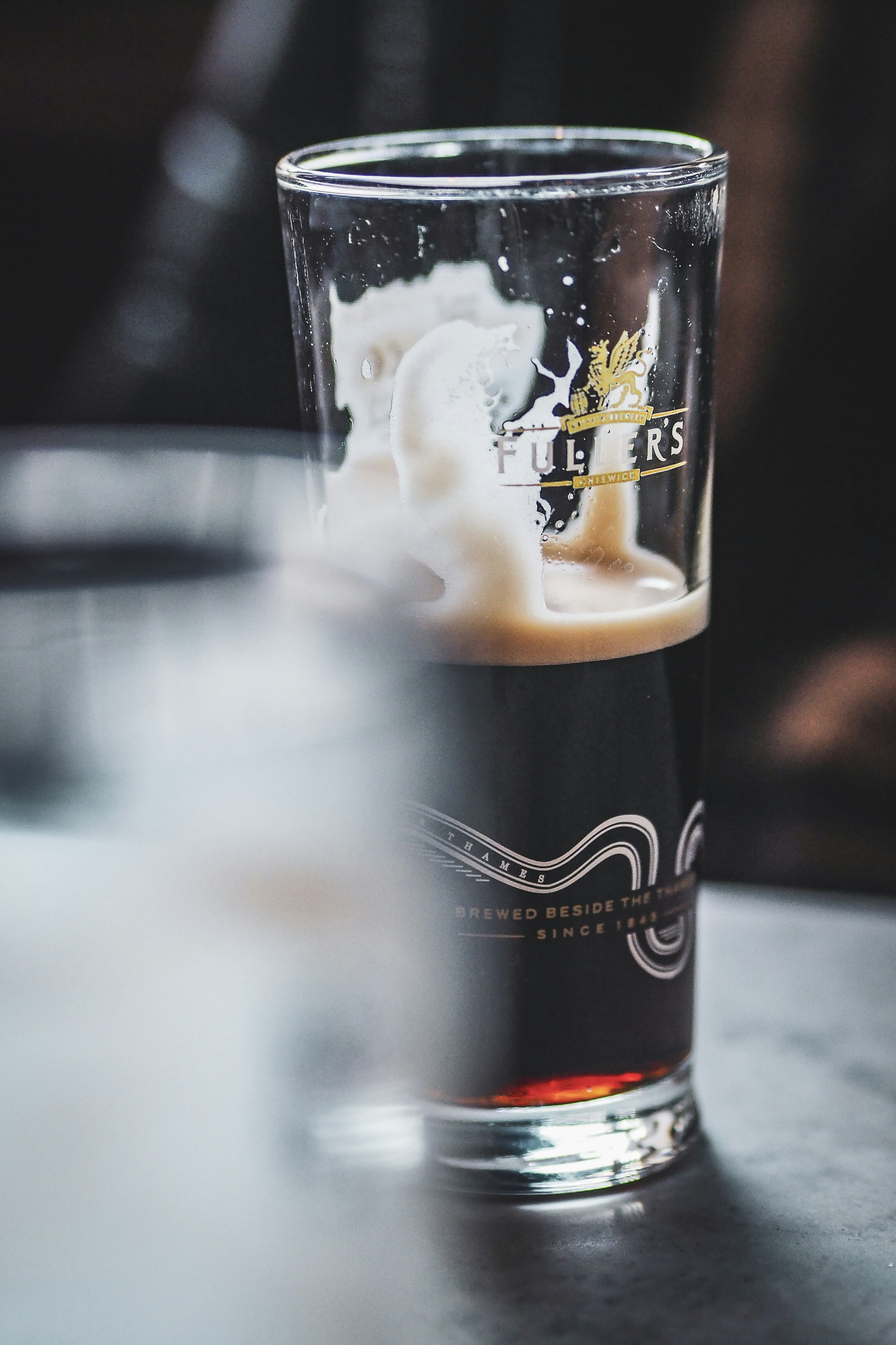 Birra scura con la testa schiumosa in un bicchiere a marchio fuller's.