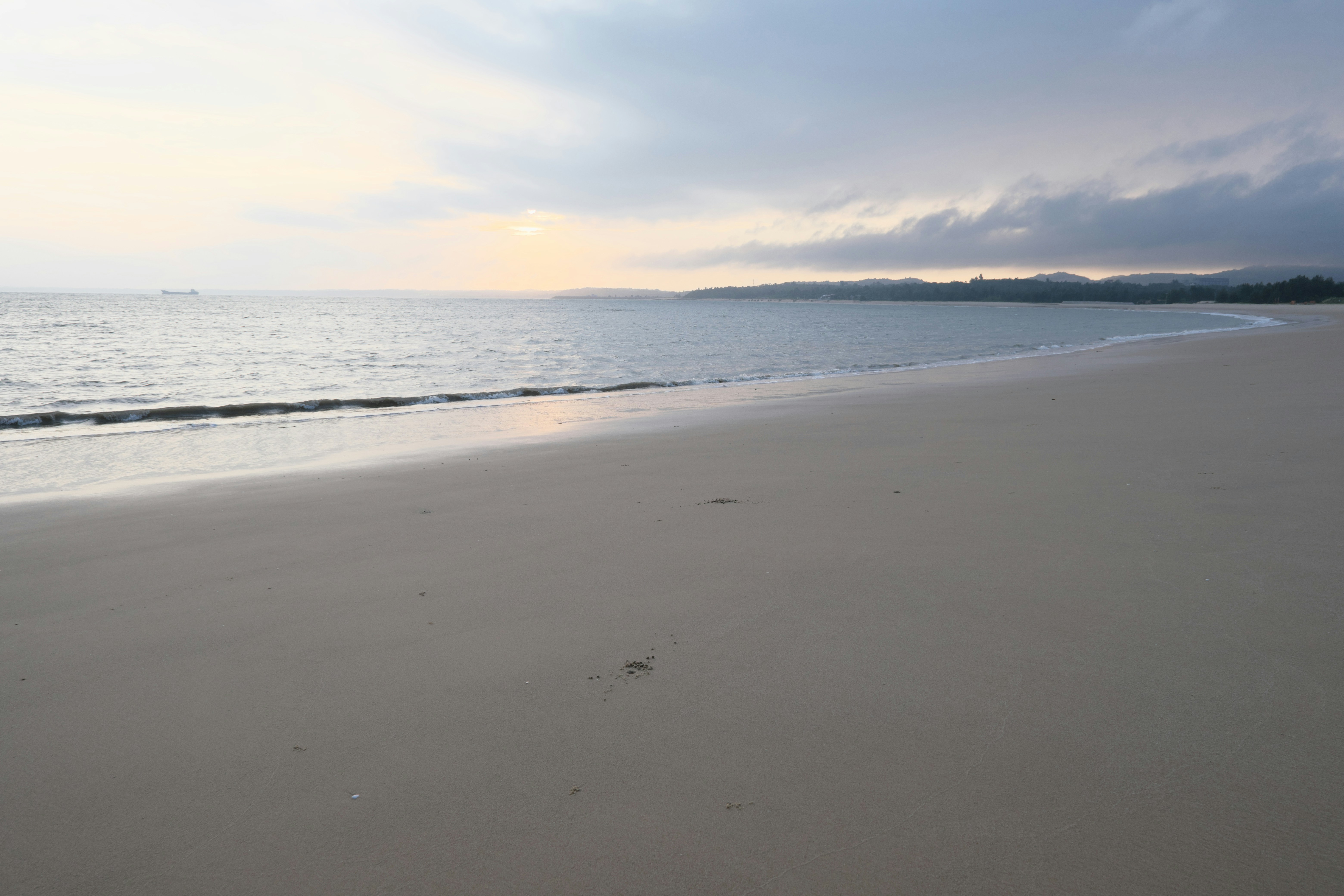 Empty sandy beach meeting the ocean under a cloudy sky