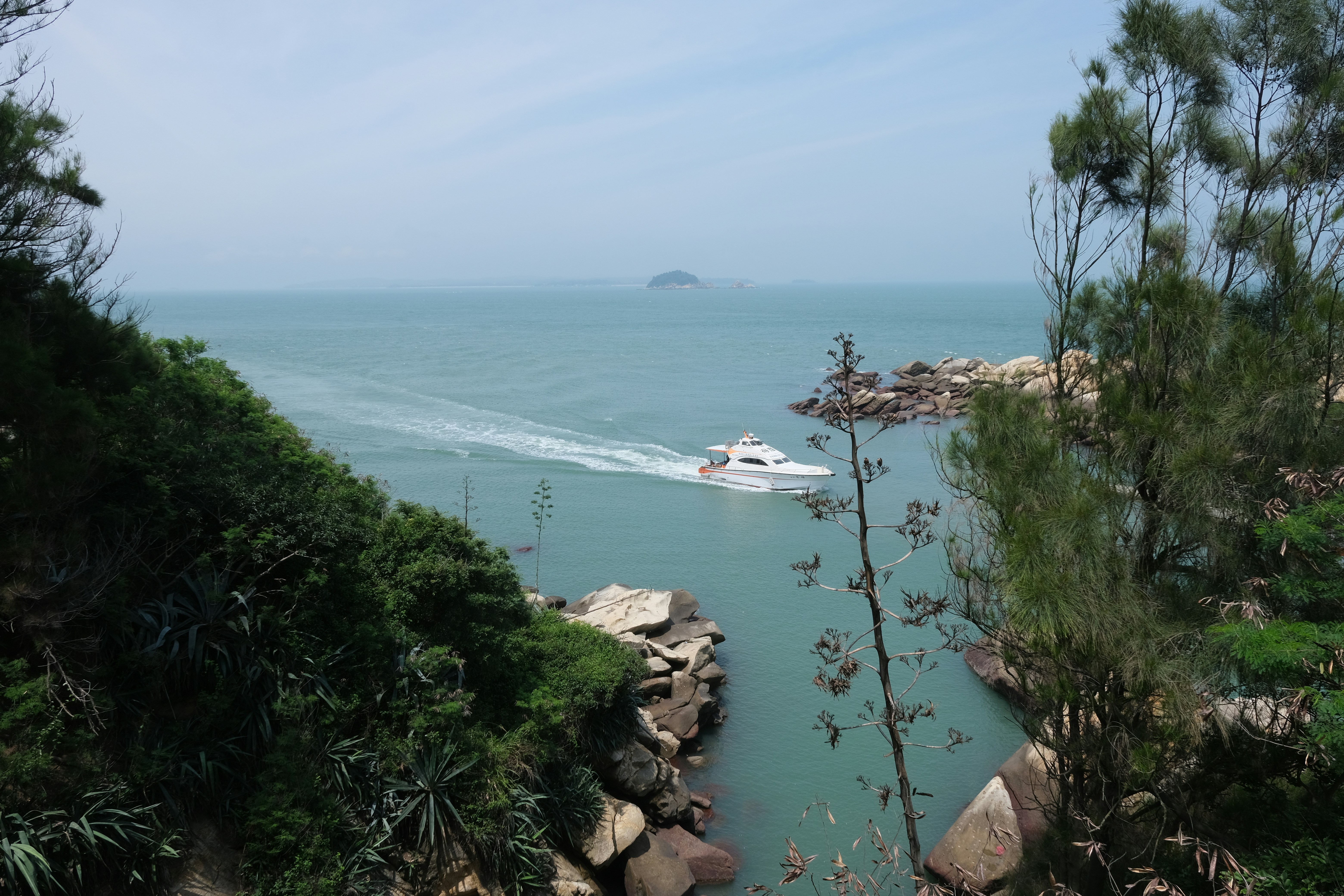 A white boat speeds through a channel between green cliffs