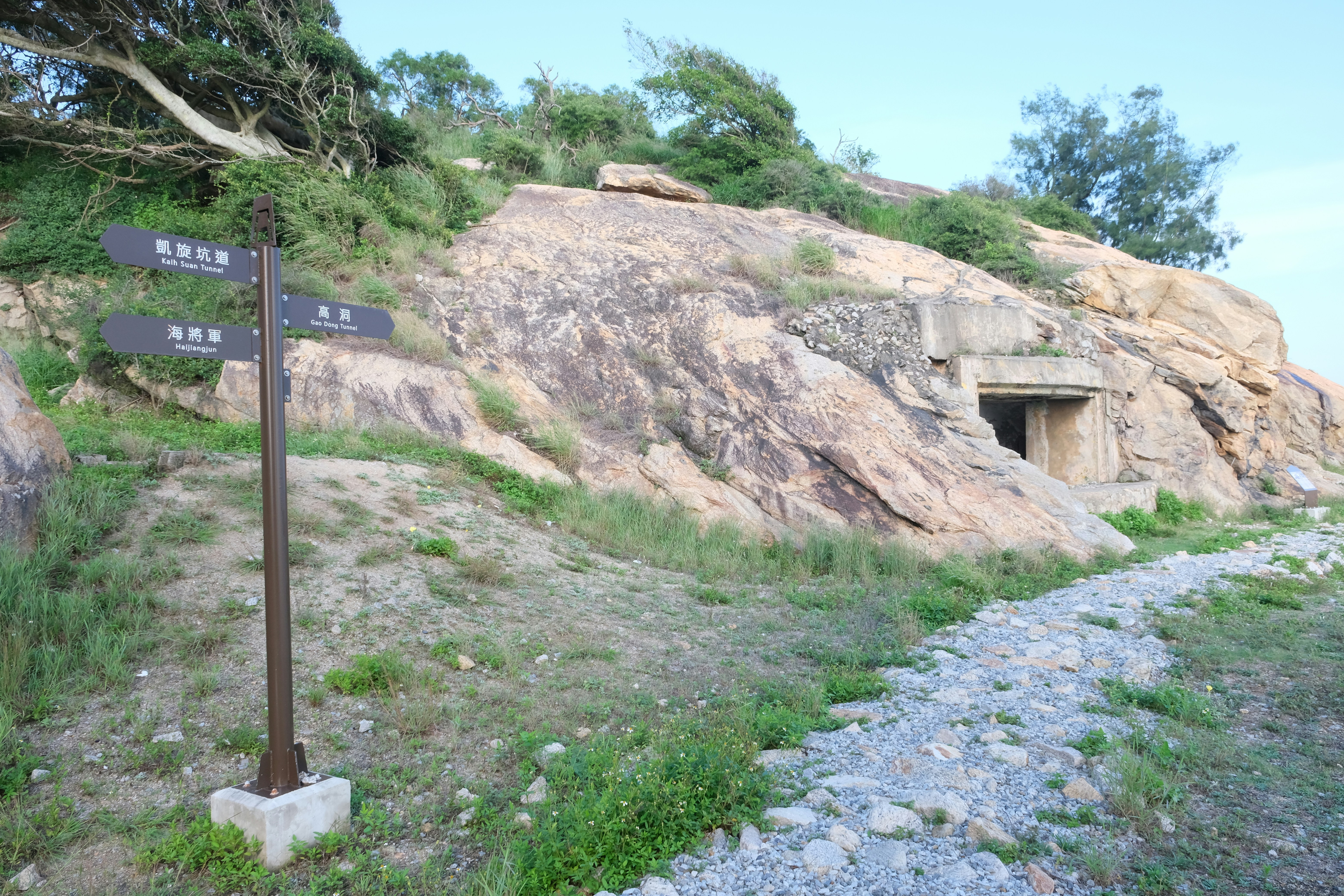 Rocky hillside with a path, signpost, and cave entrance