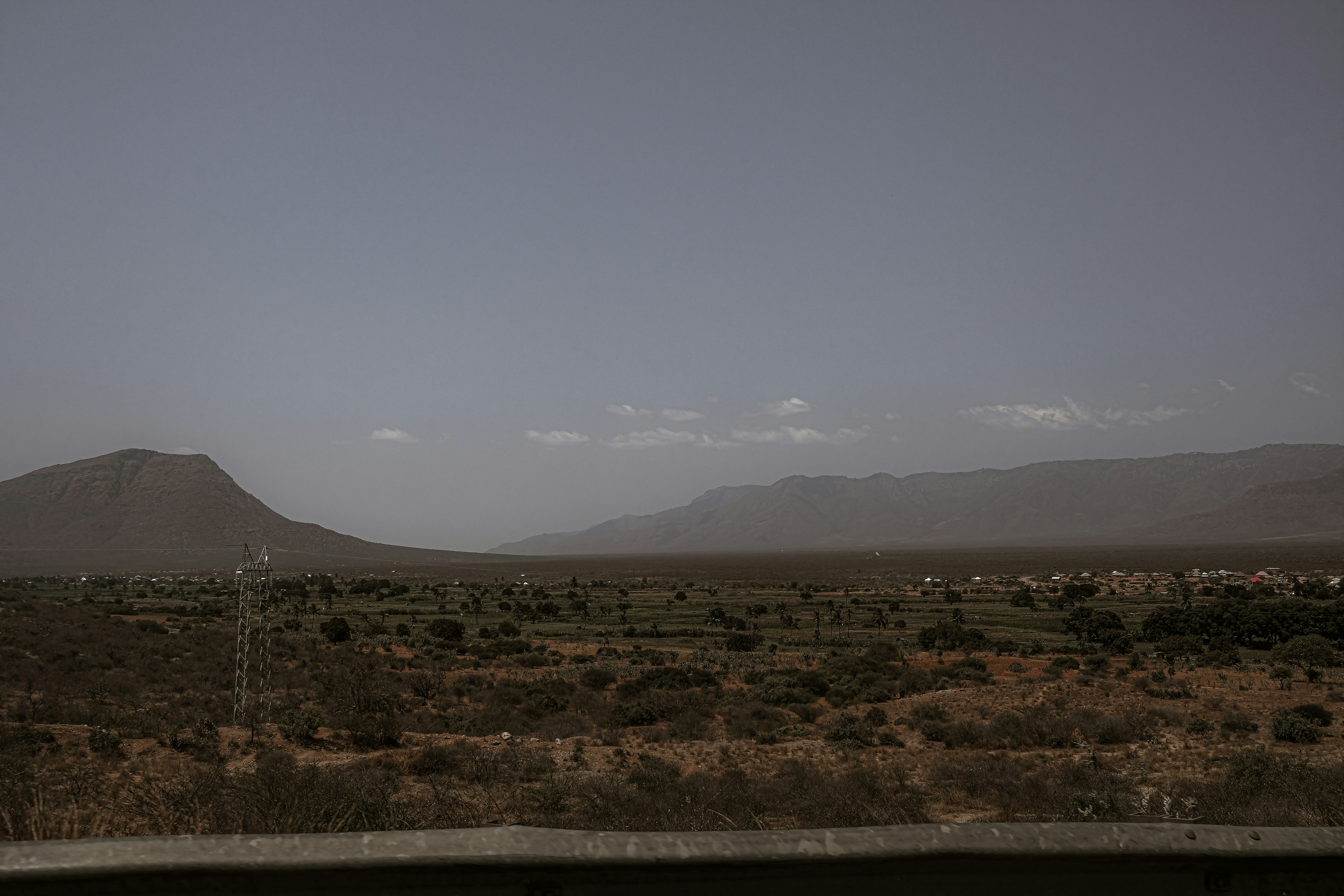 Dry rural landscape with distant mountains under a hazy sky.