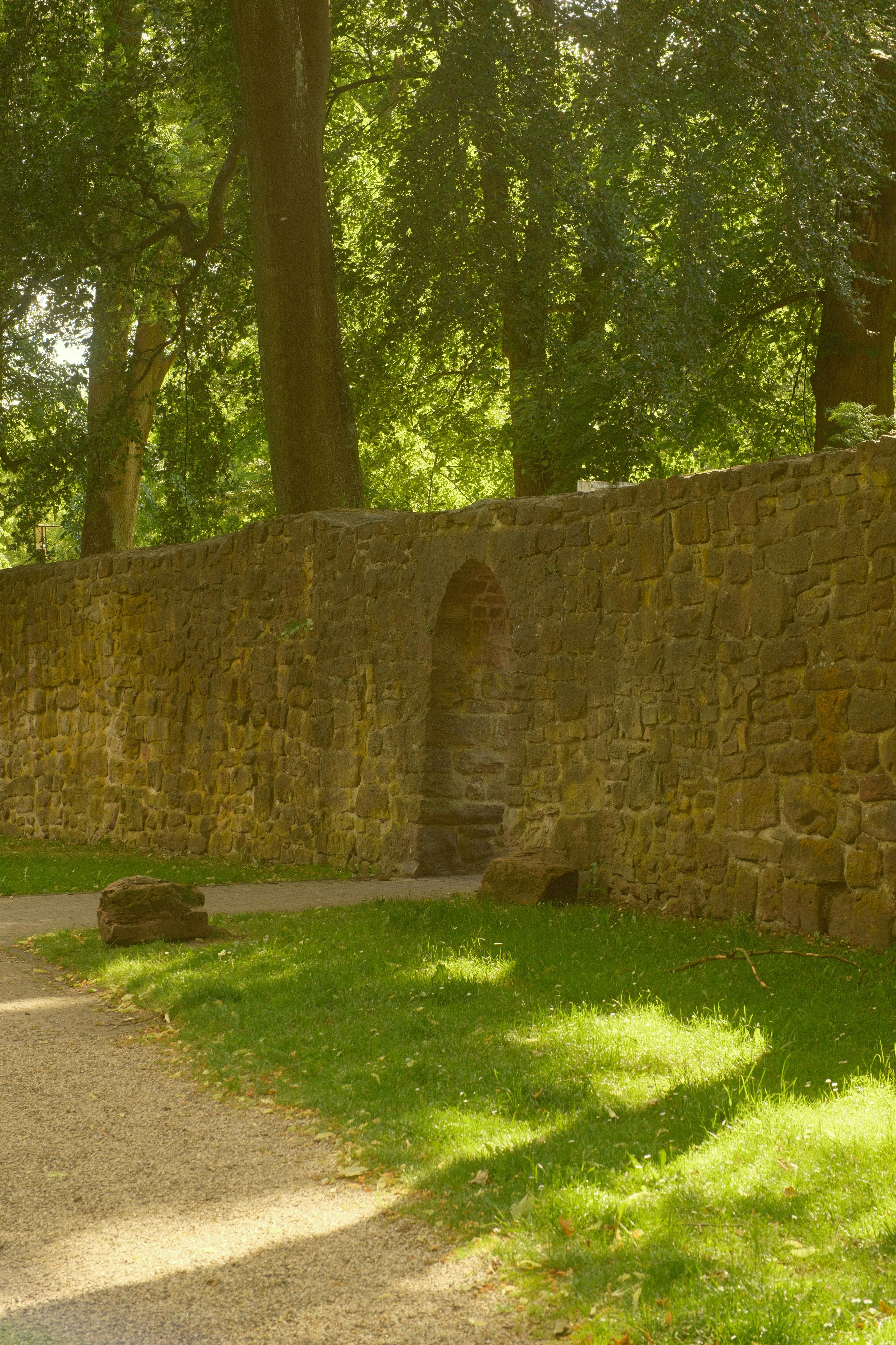 Mur de pierre avec passage voûté et chemin ensoleillé.