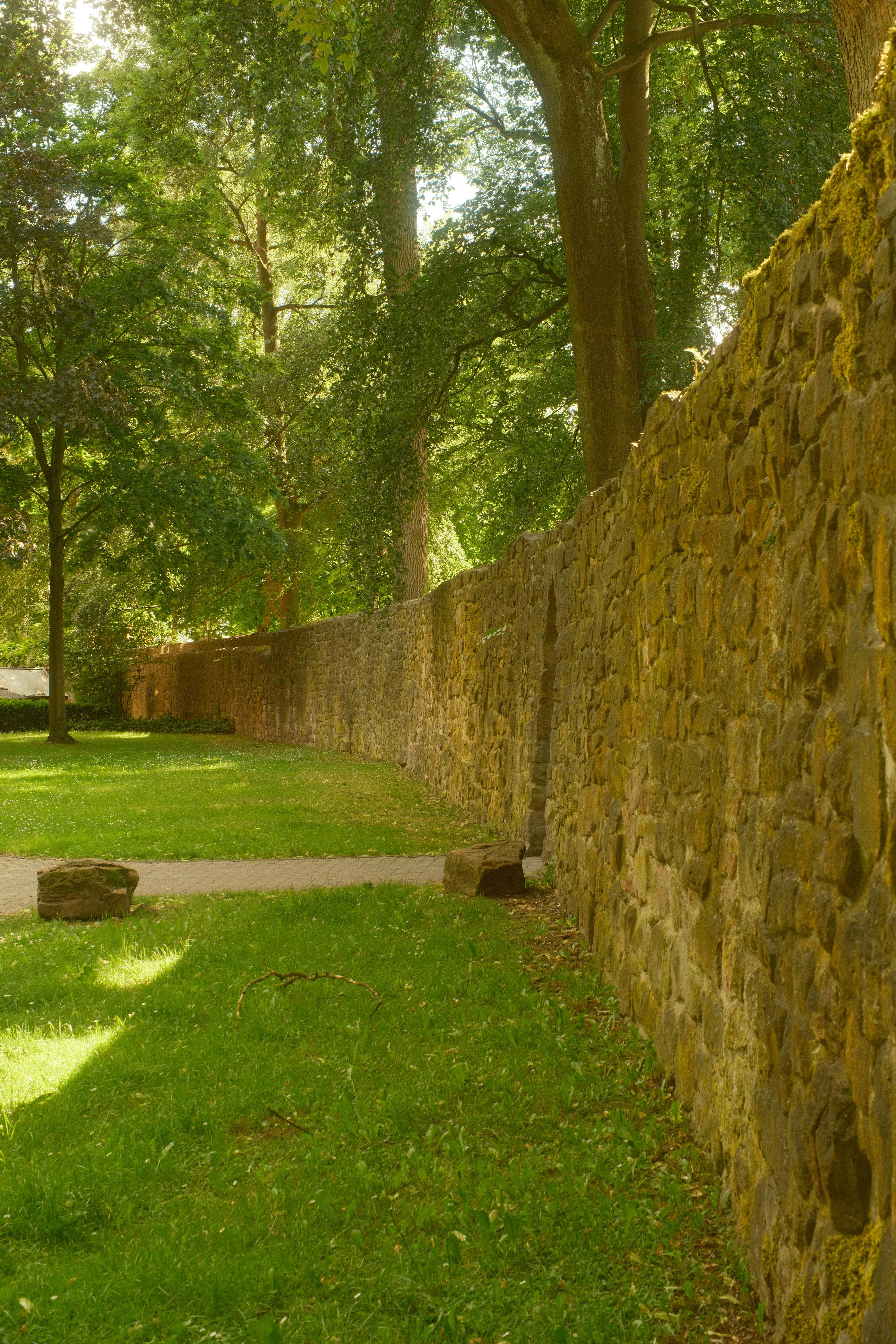 Un long mur de pierre et une pelouse verte dans un parc ensoleillé.