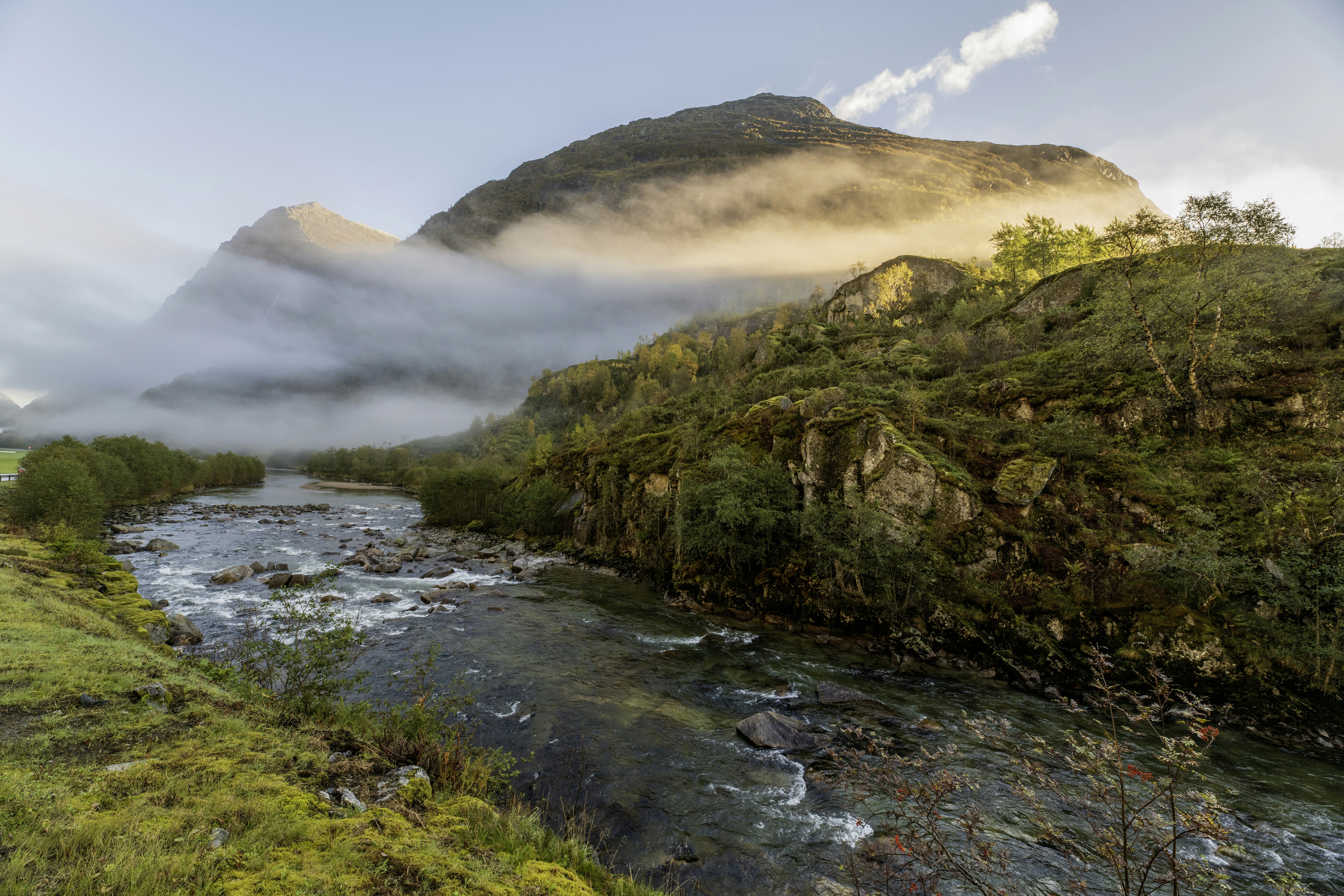 A river flows through a misty mountain landscape at sunrise.