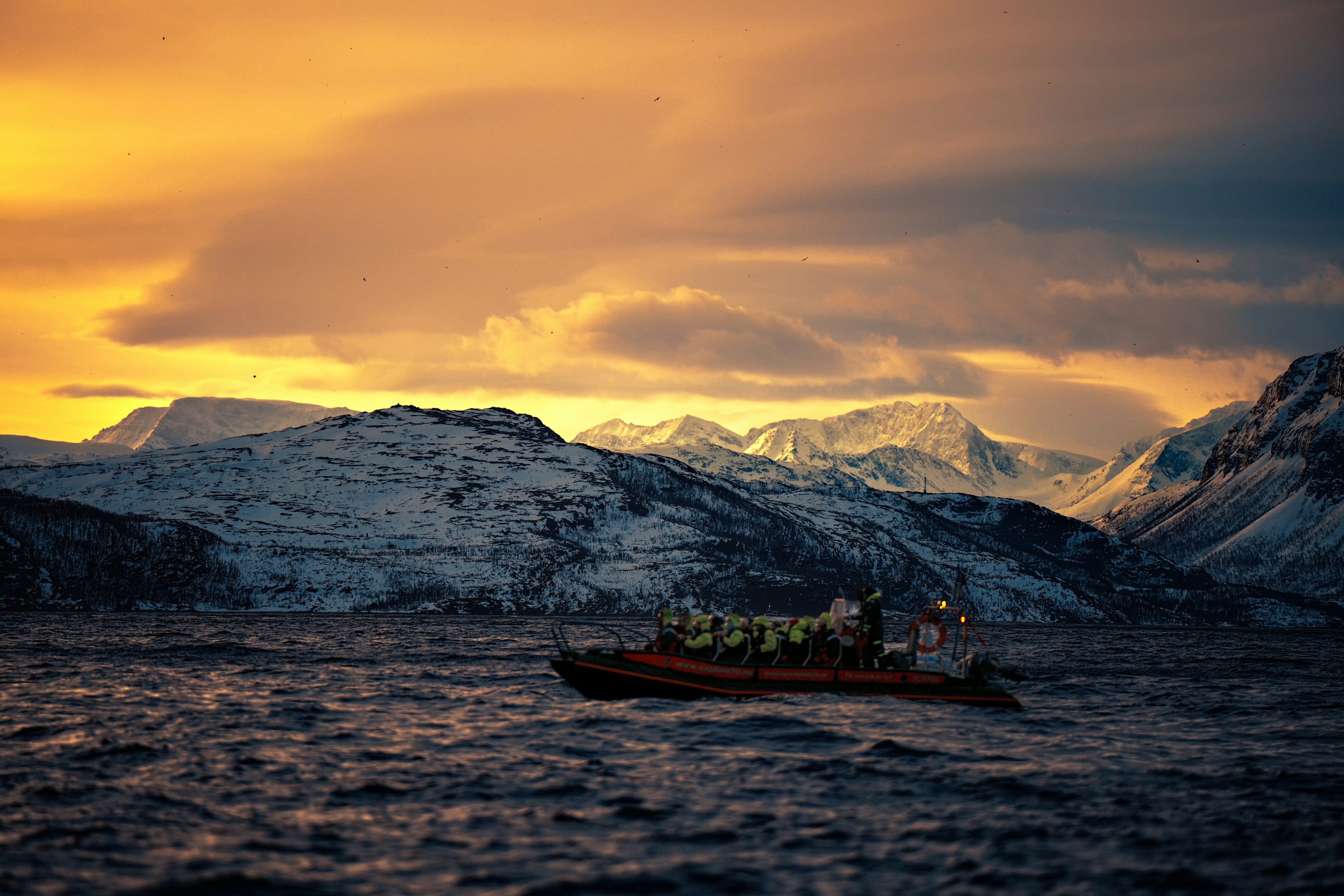 A boat navigates choppy water near snowy mountains at sunset