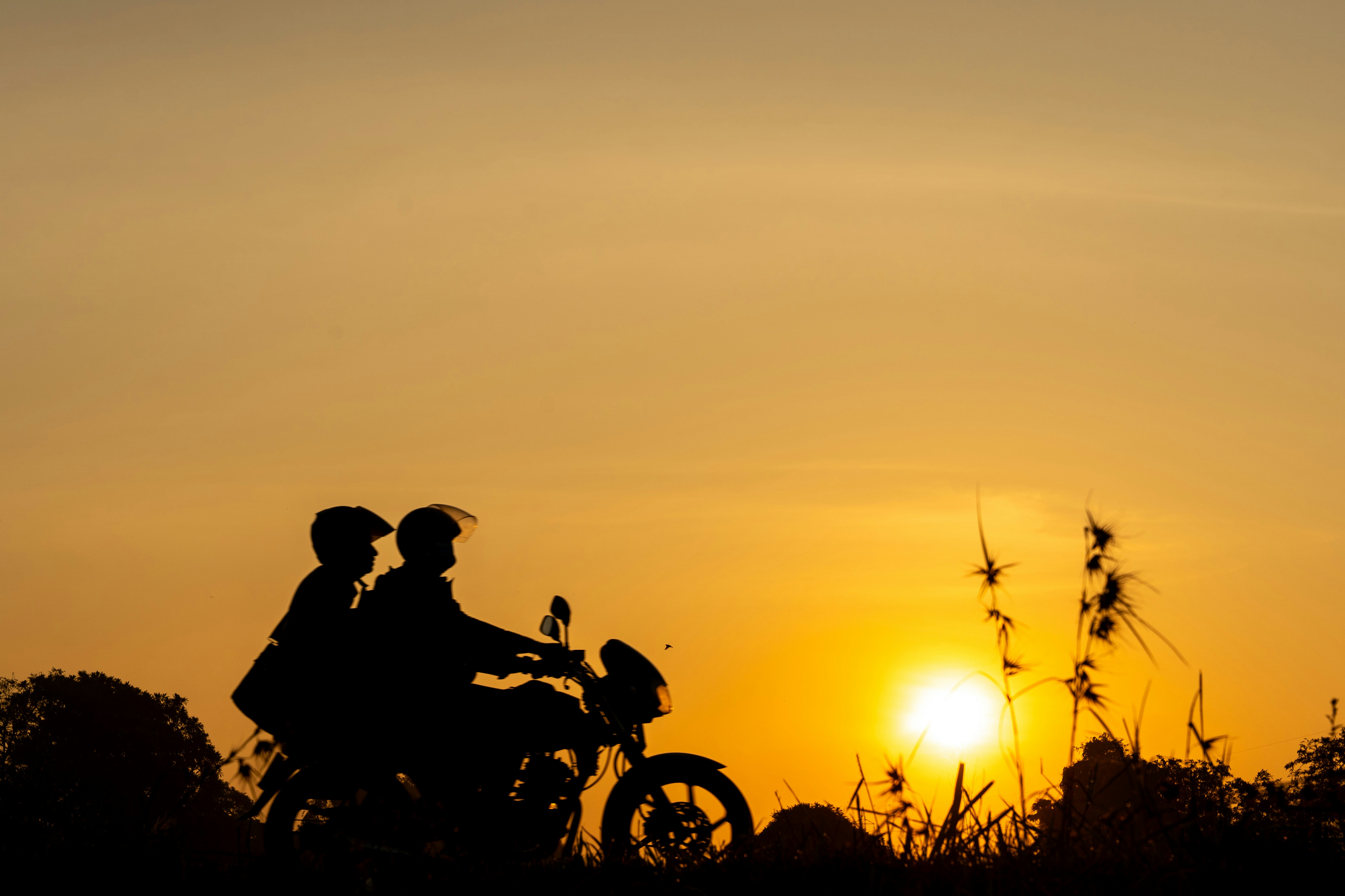 Silhouette of two people on a motorcycle at sunset.