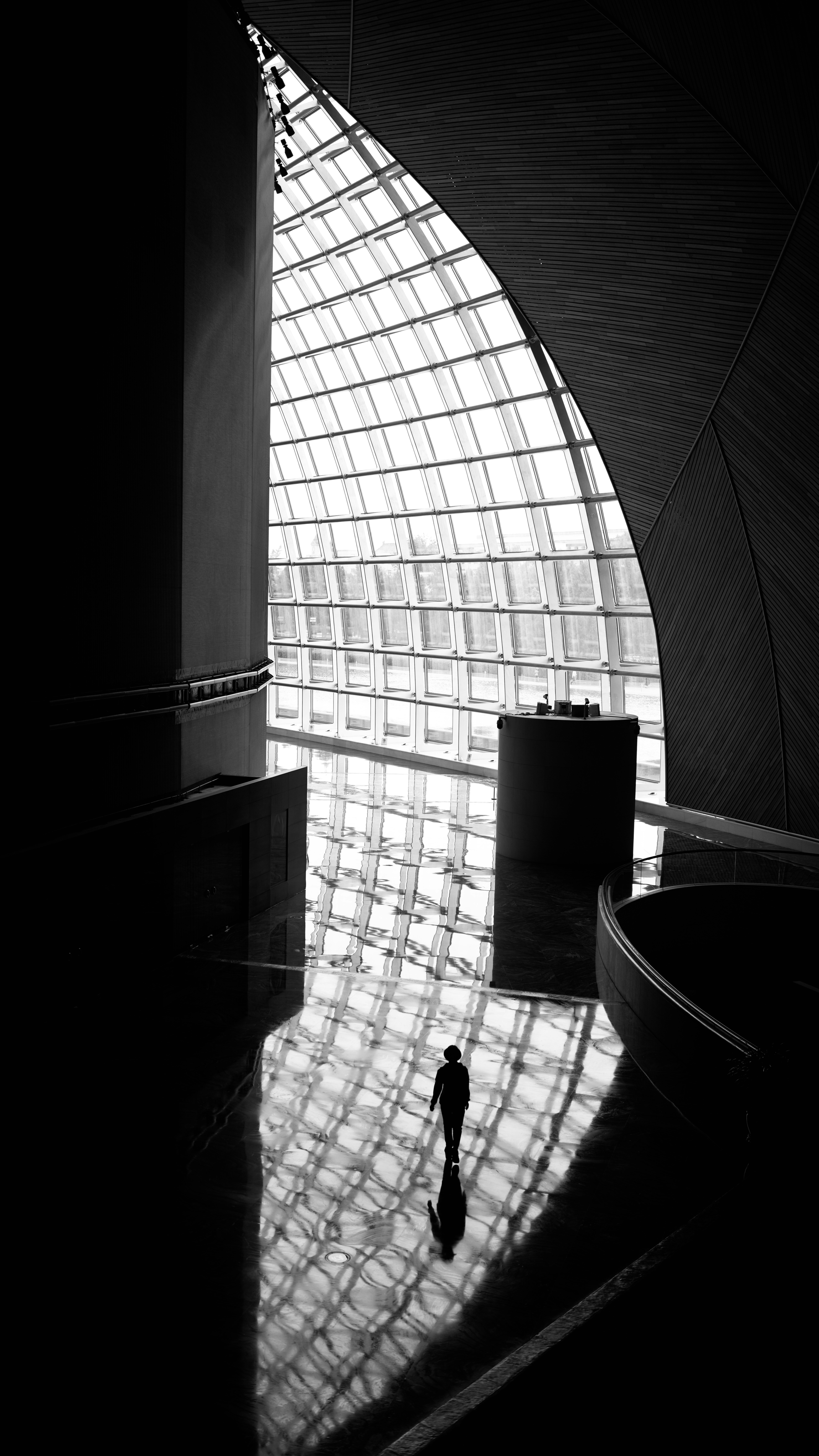 Silhouetted figure walks on reflective floor of modern building.
