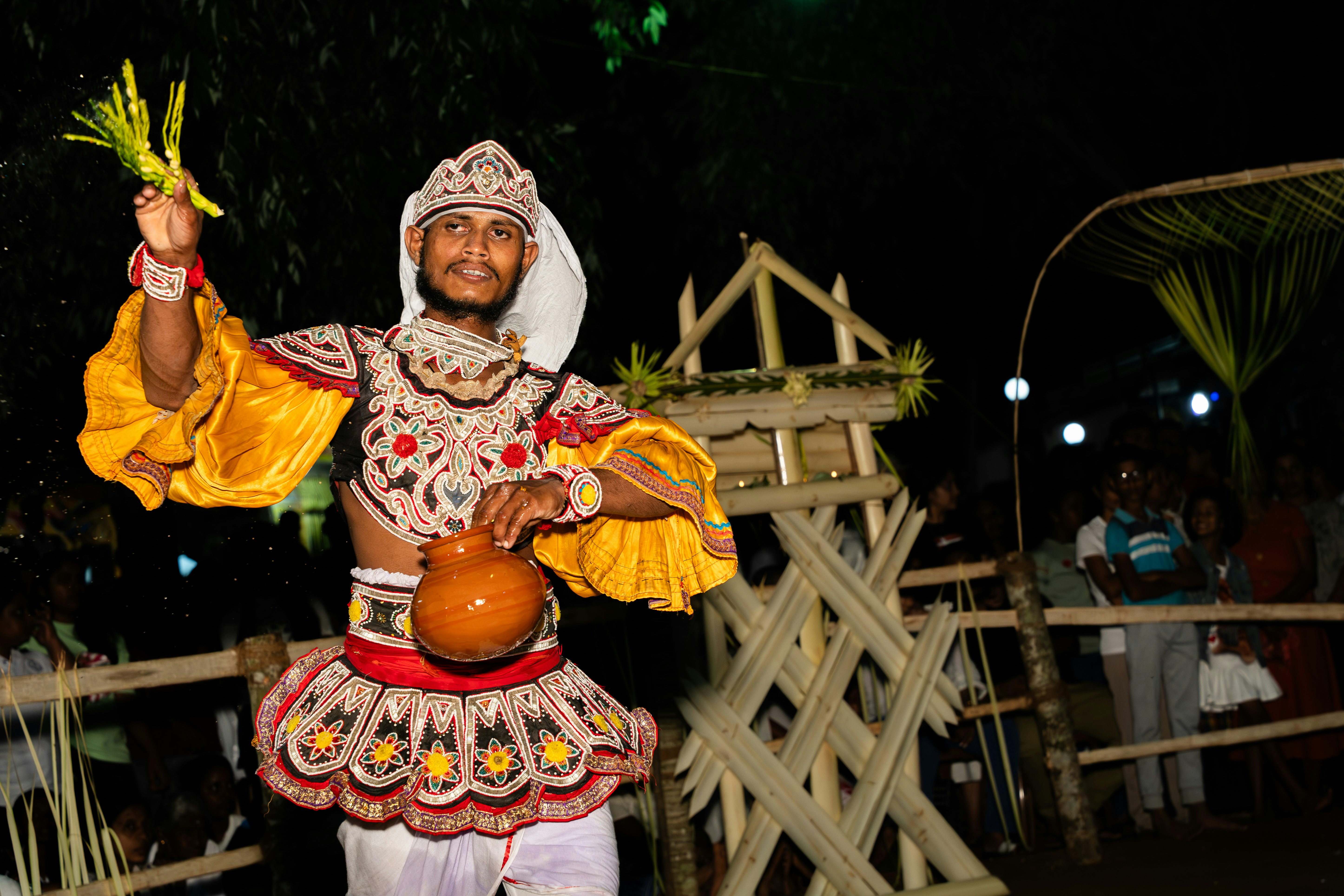 Traditional dancer in ornate costume holding leaves and a pot.