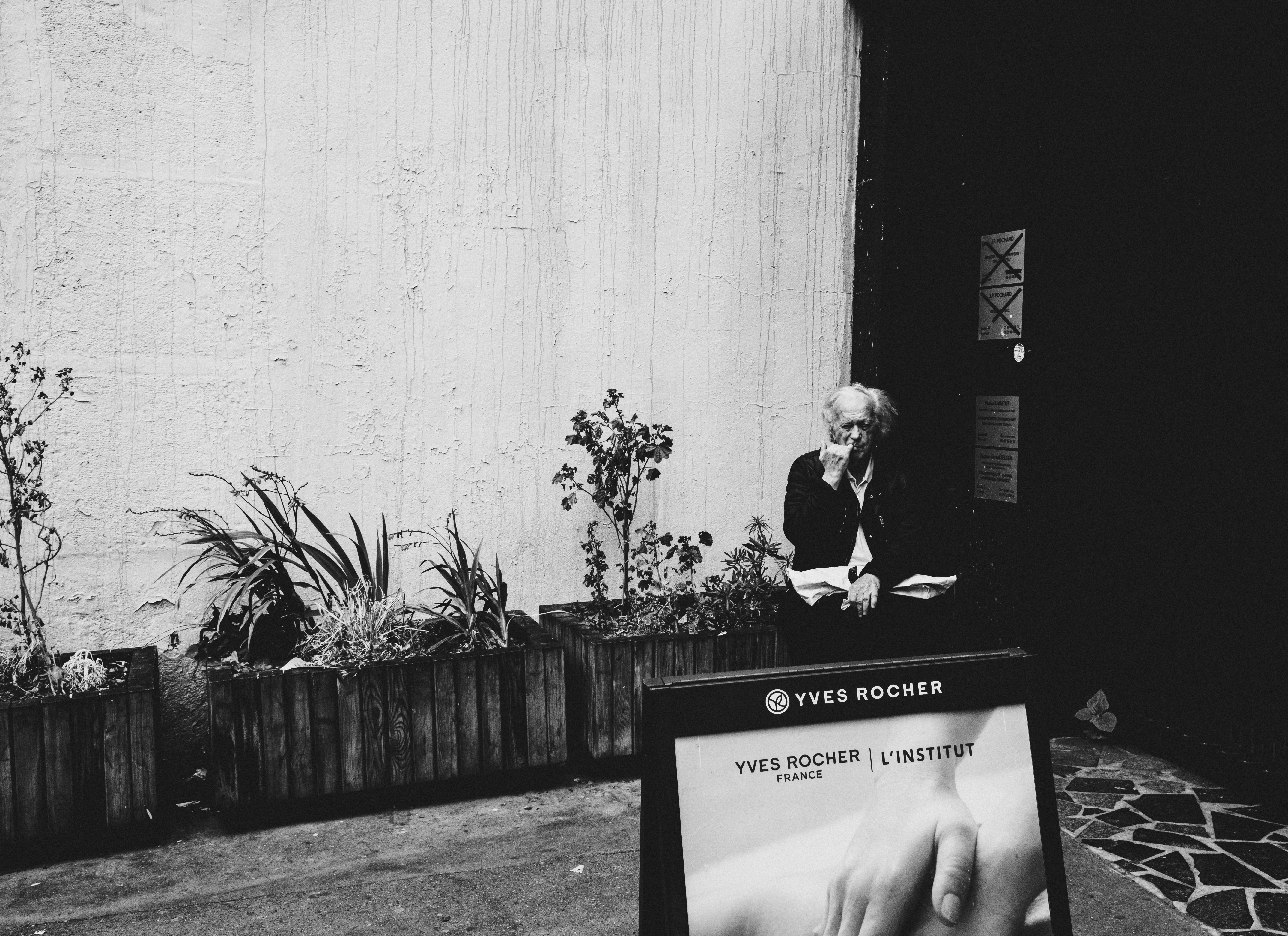 Black and white outdoor scene with person, plants, and sign.
