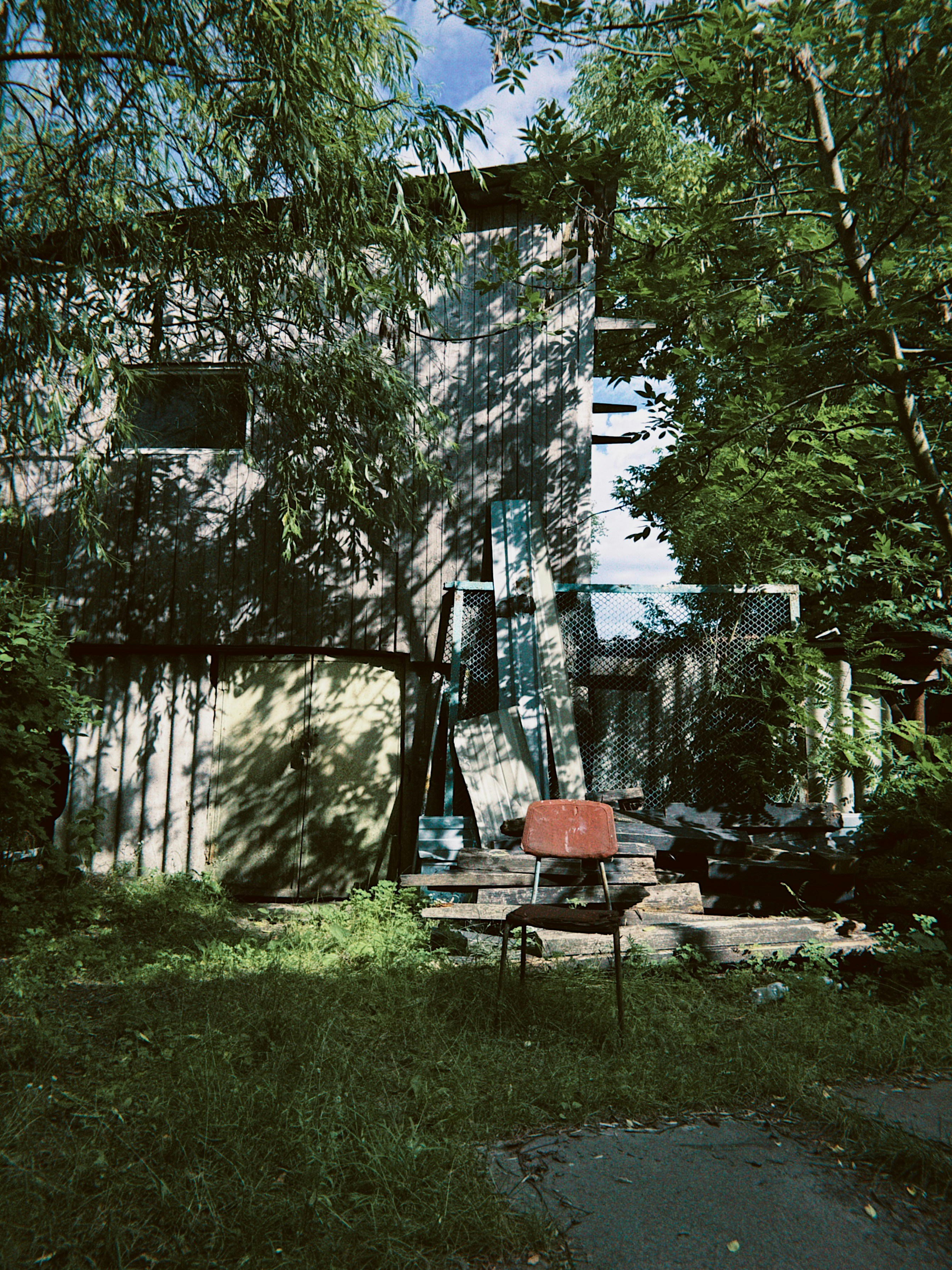 Dilapidated building with an old orange chair and overgrown foliage.