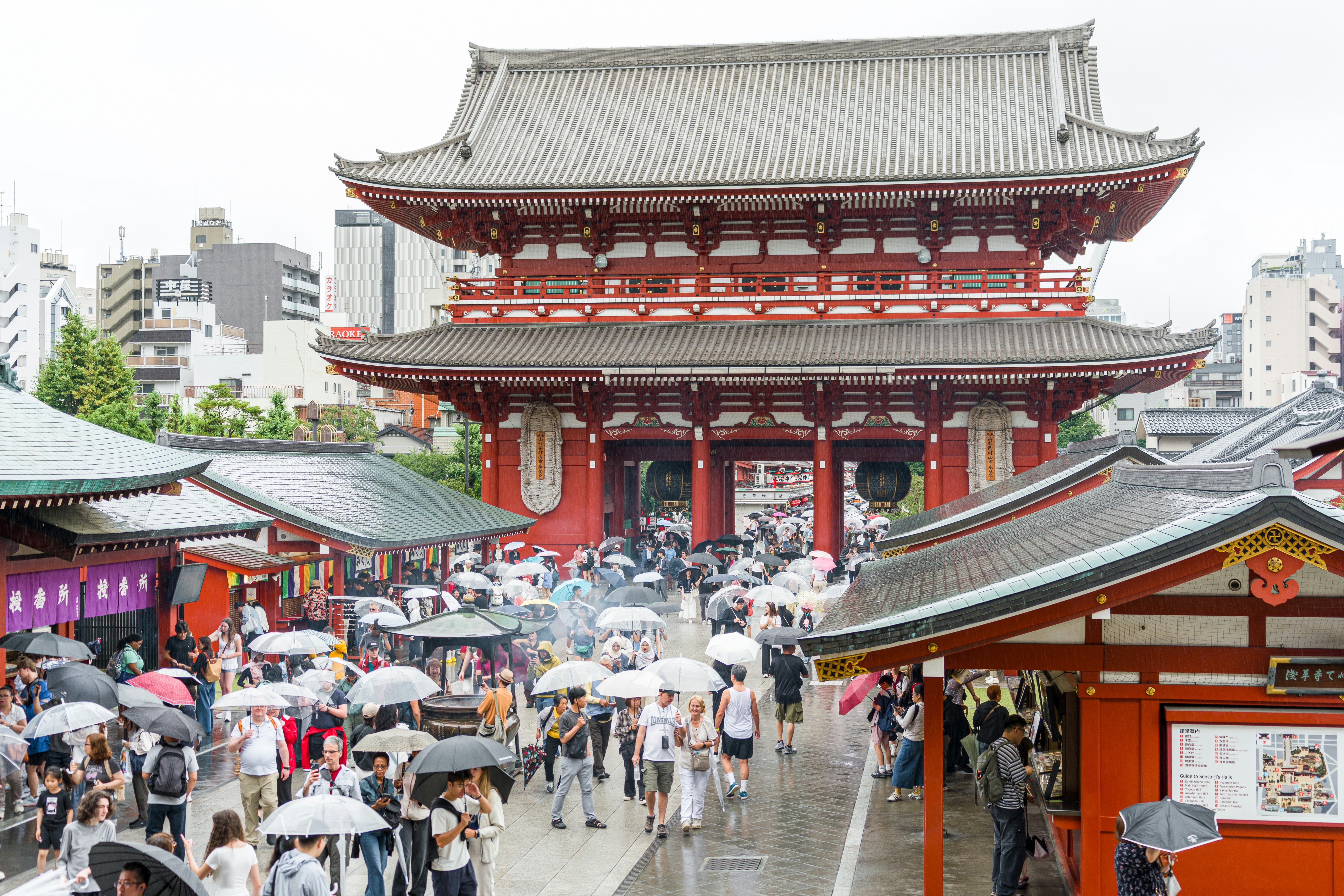 Visitors with umbrellas at a traditional japanese temple gate.