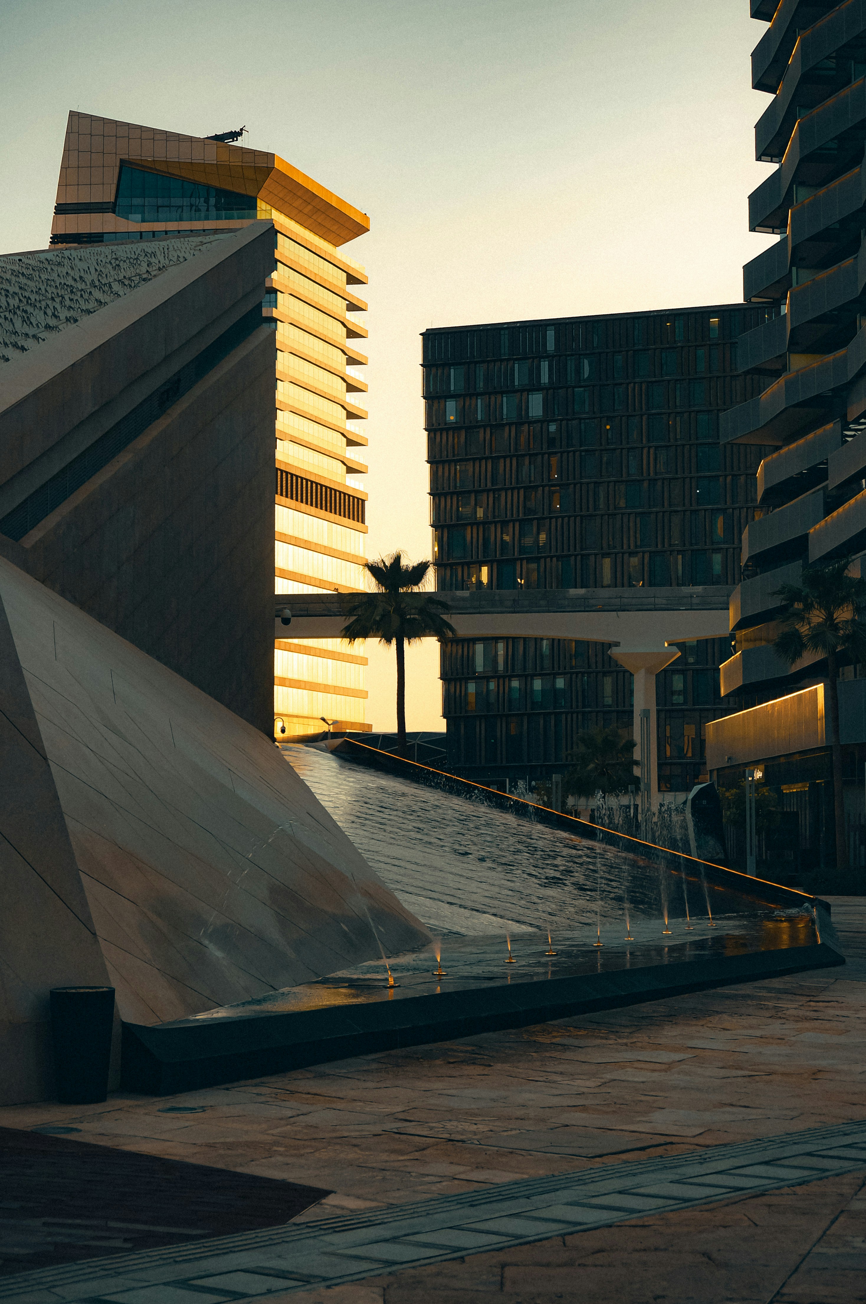Golden hour light on modern buildings and a geometric fountain.