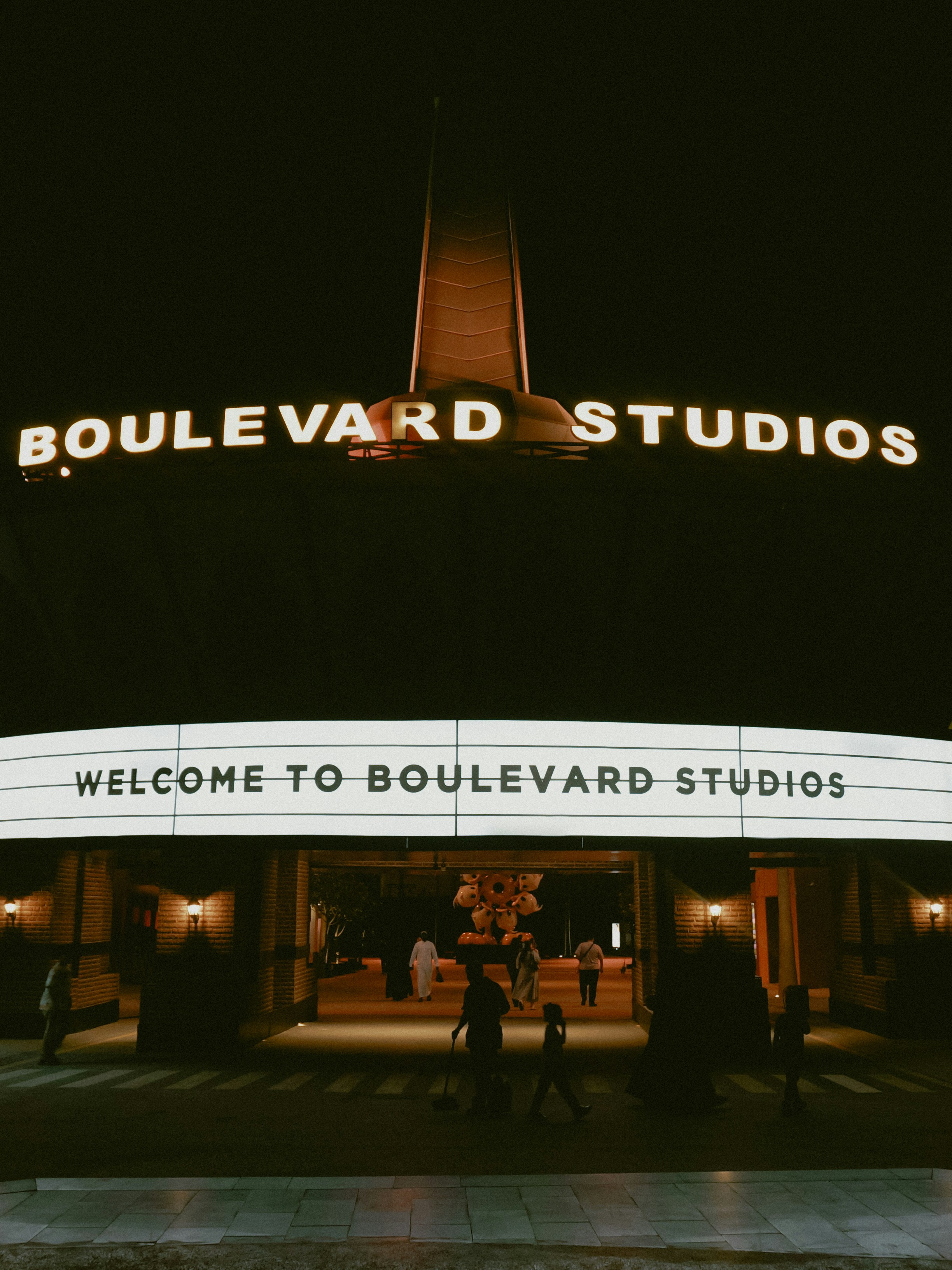 Illuminated boulevard studios entrance at night with people below.
