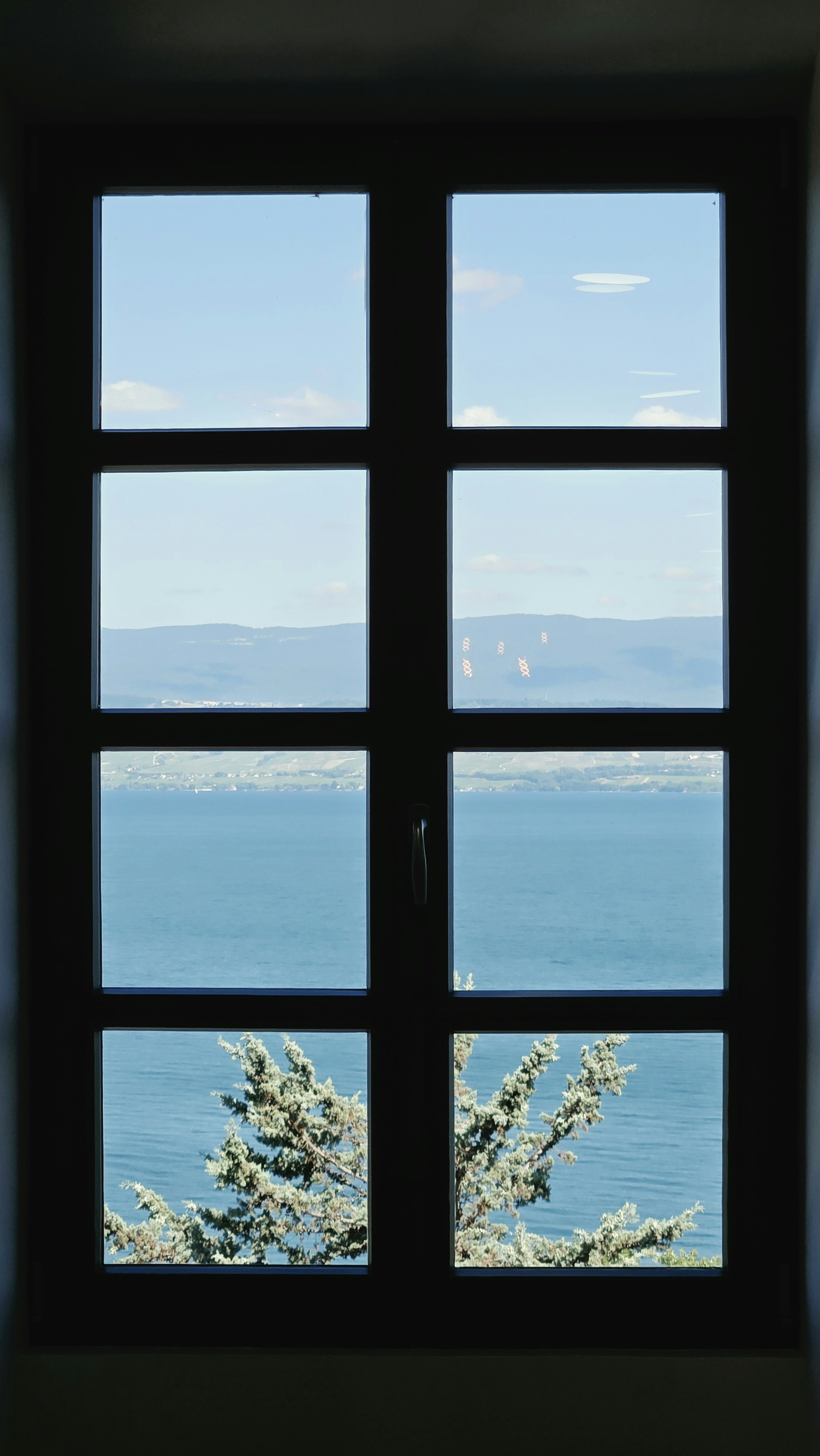 Window overlooking a serene lake with distant mountains and trees.