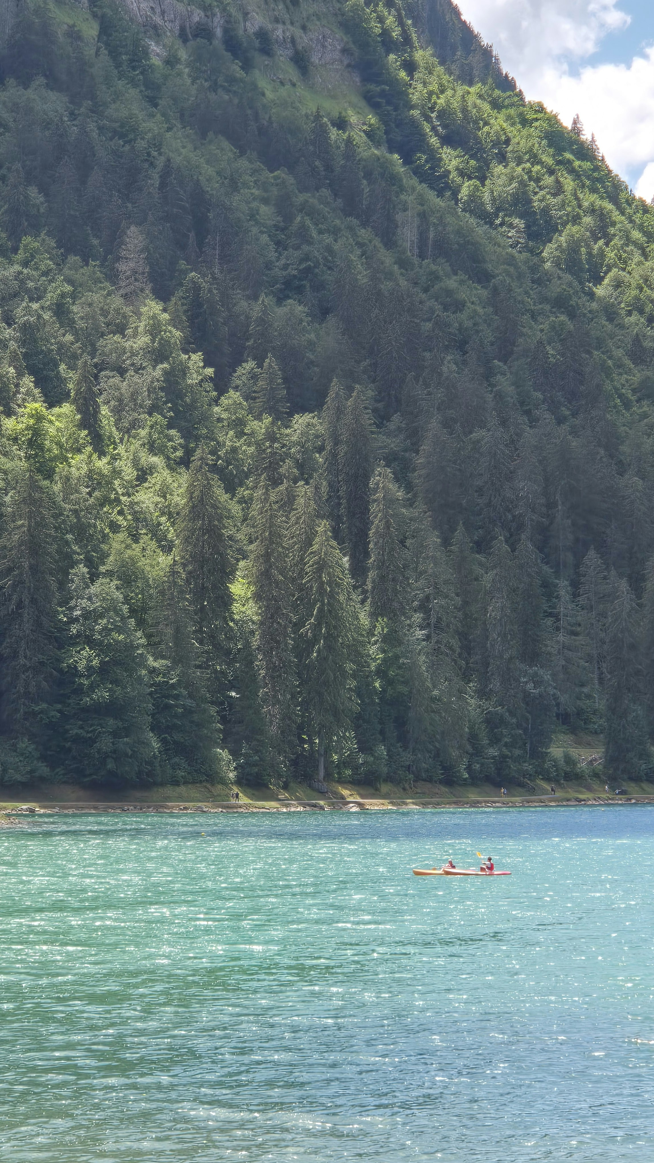 People kayaking on a lake with a forested mountain backdrop.