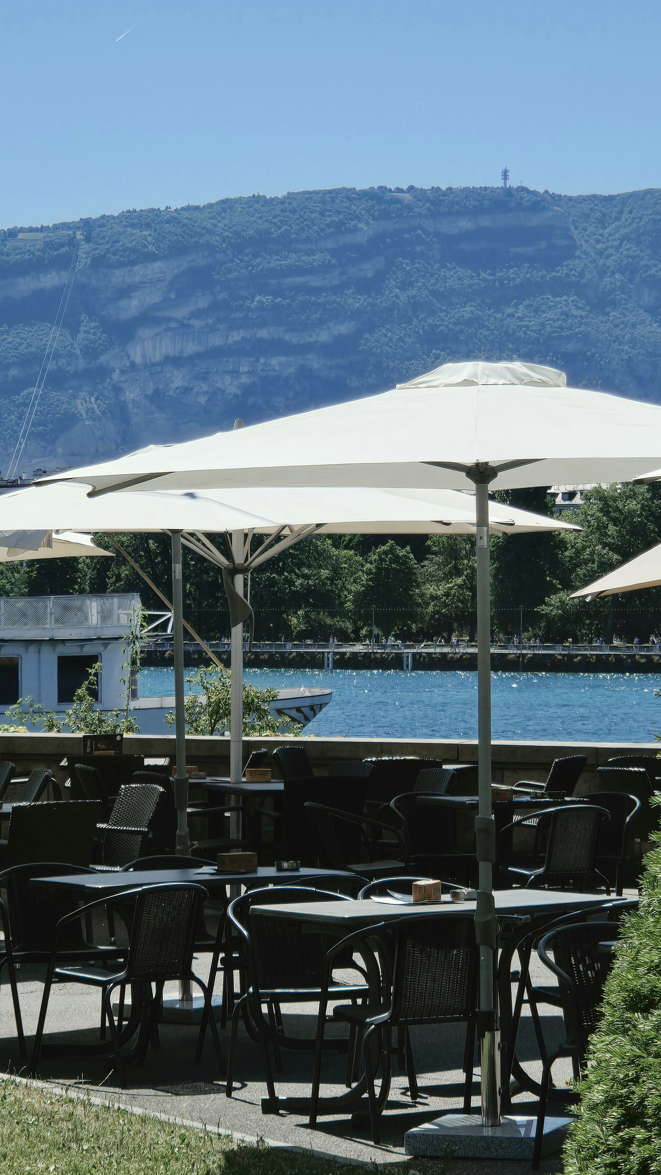 Outdoor cafe with white umbrellas by a lake and mountains.