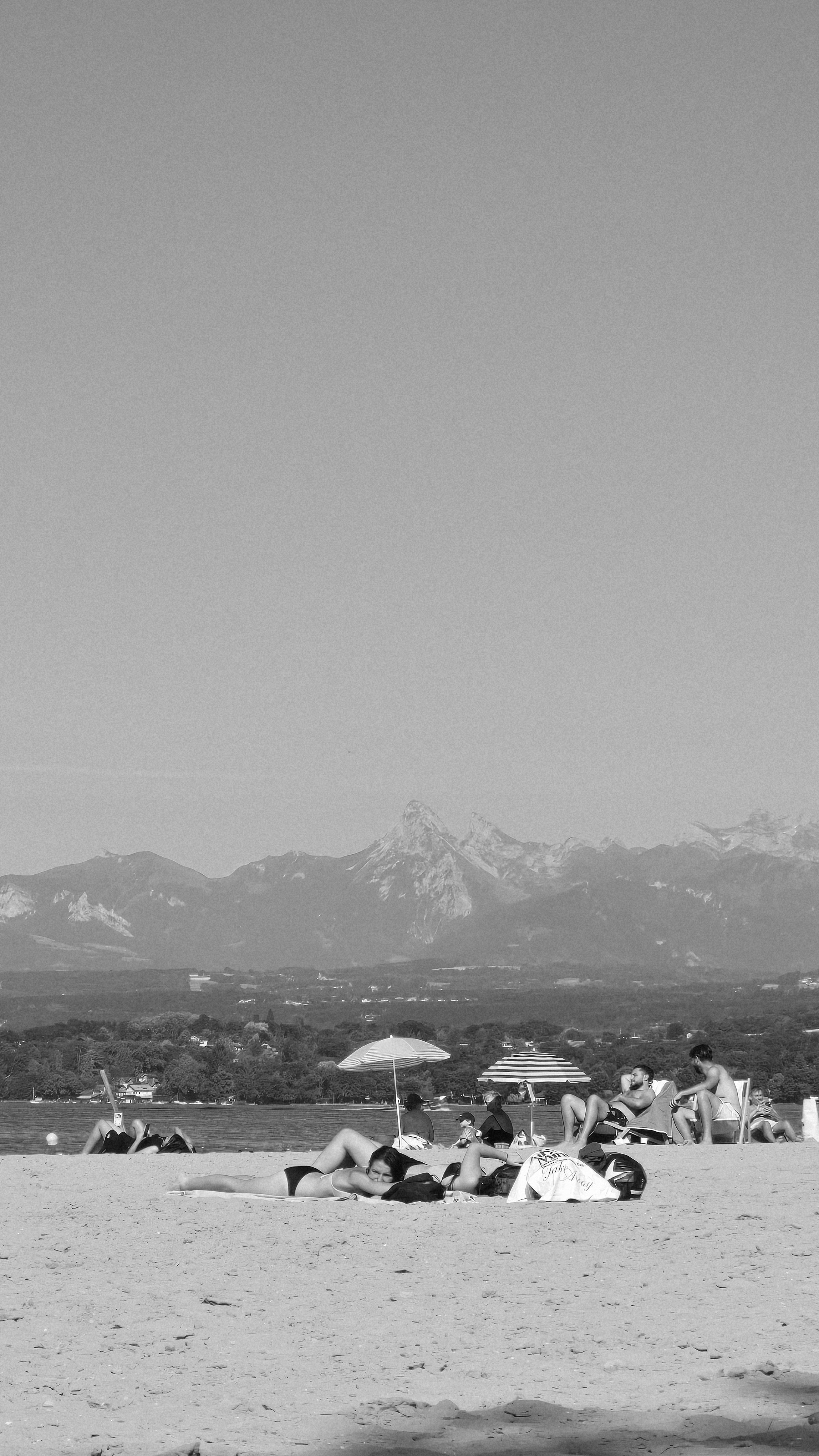 People relaxing on a sunny beach with distant mountains.