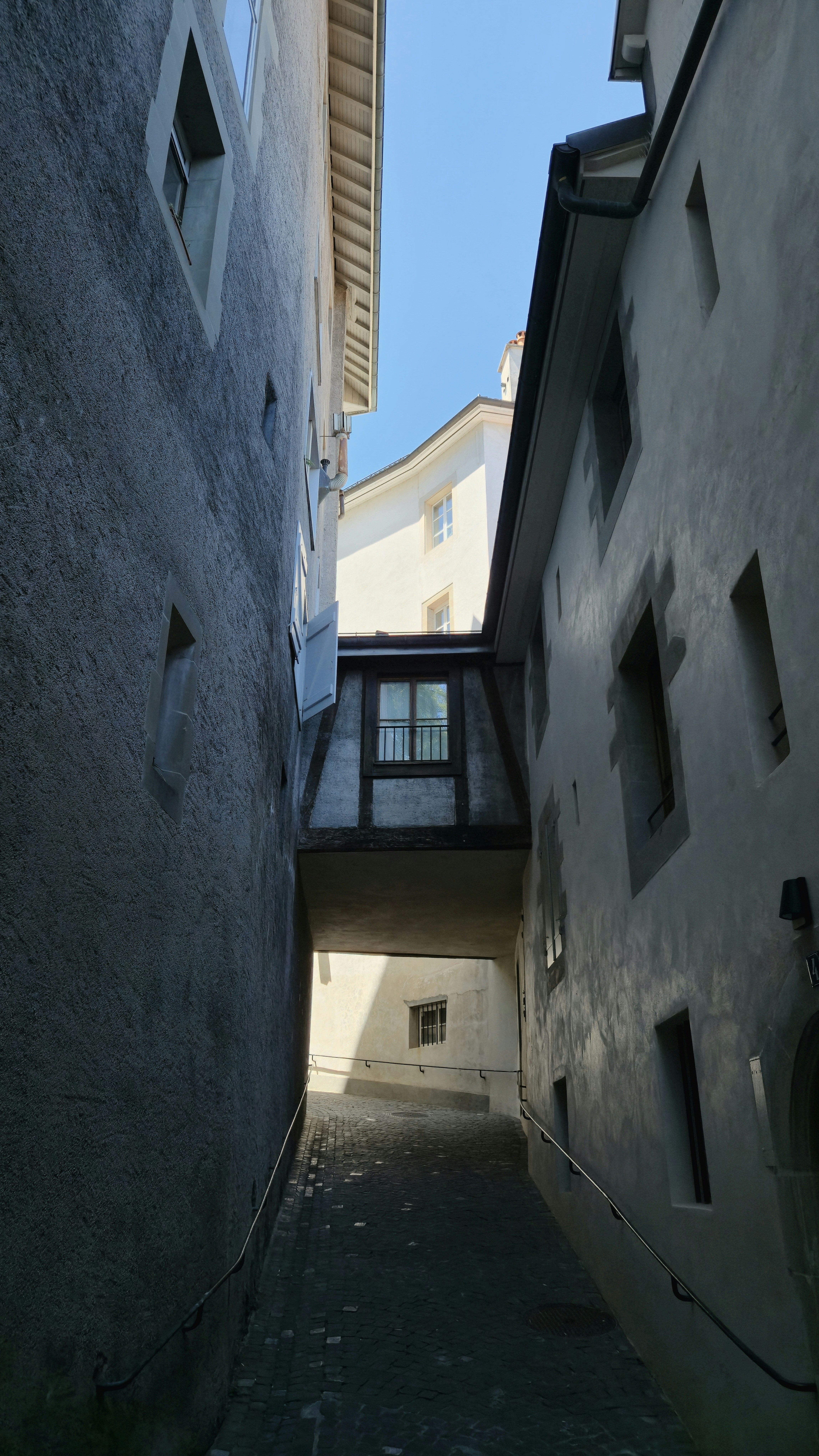 Steep, shadowed alleyway with an enclosed bridge overhead.