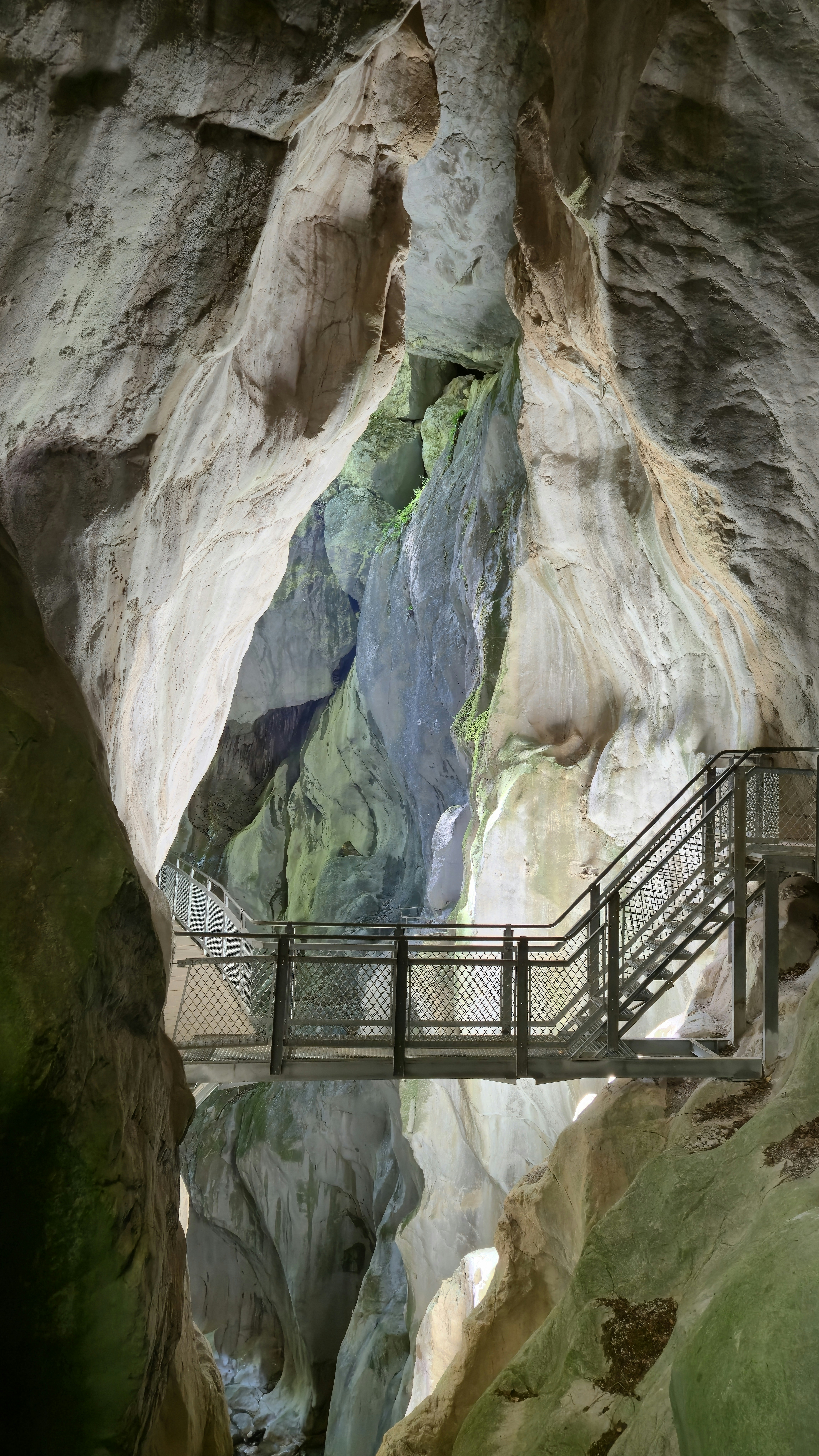 Elevated metal walkway and stairs in a narrow canyon.