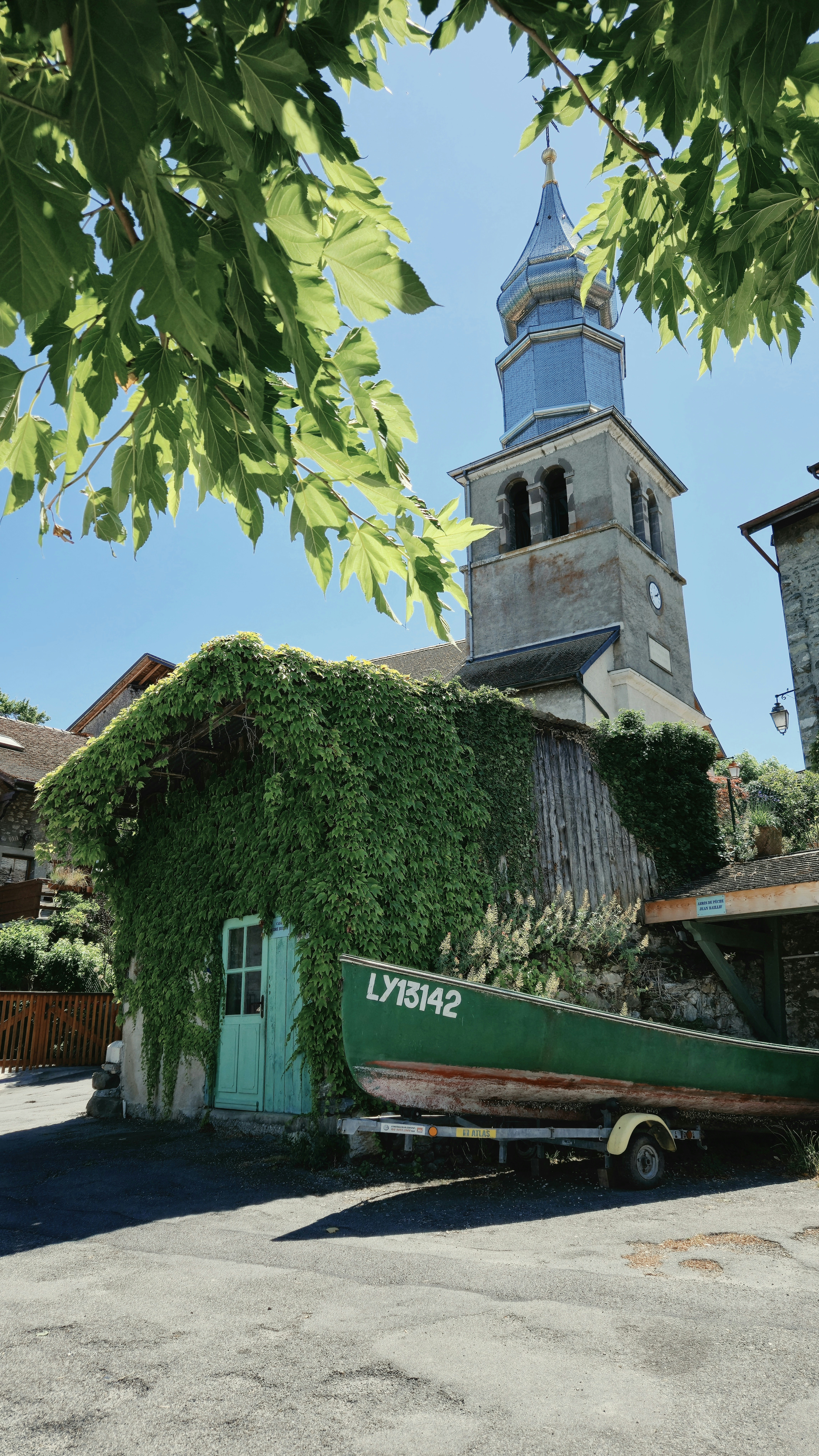 A church, ivy-covered building, and green boat under blue sky.