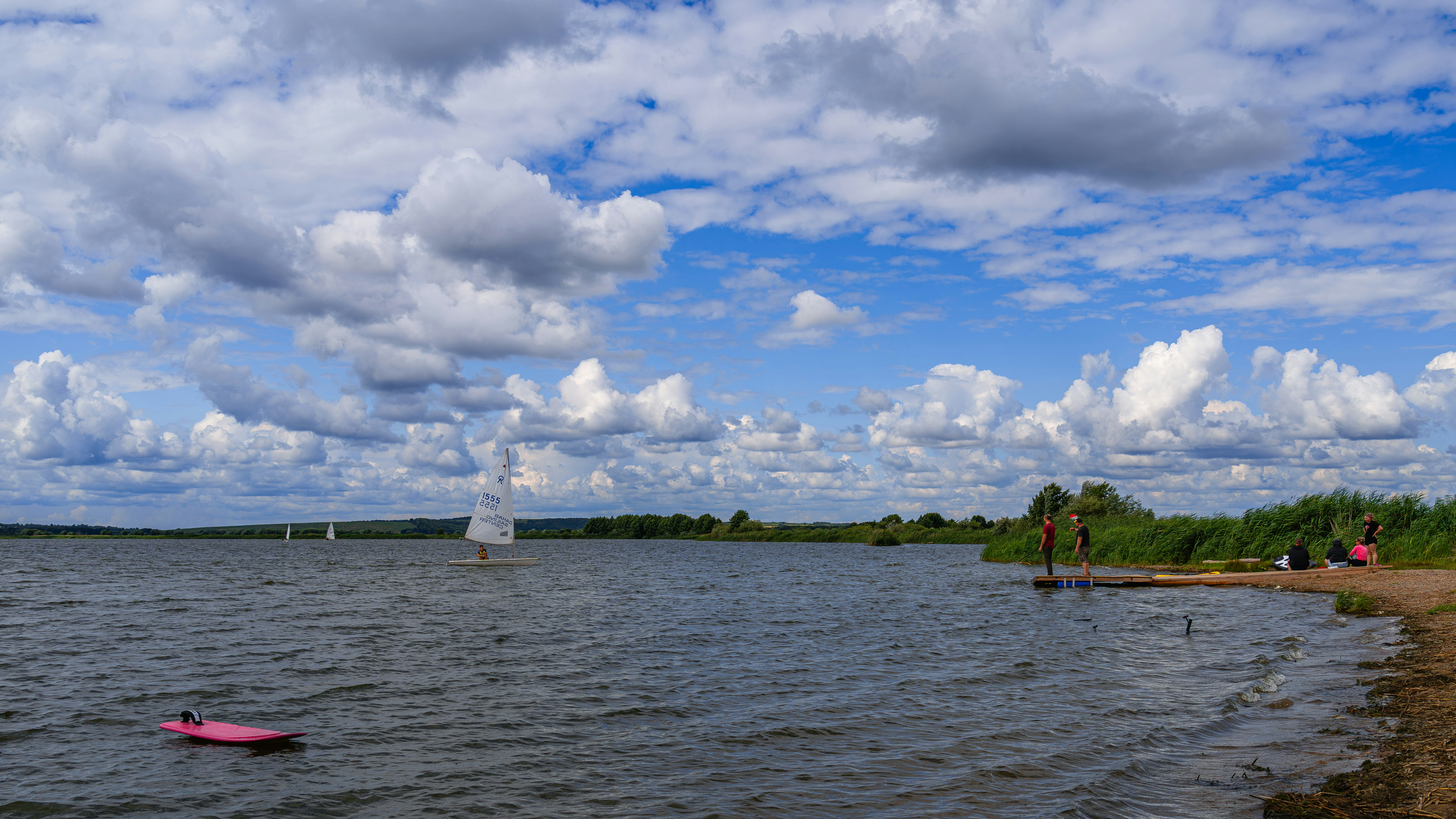 See mit Segelbooten, sandigem Ufer und wolkigem blauen Himmel.