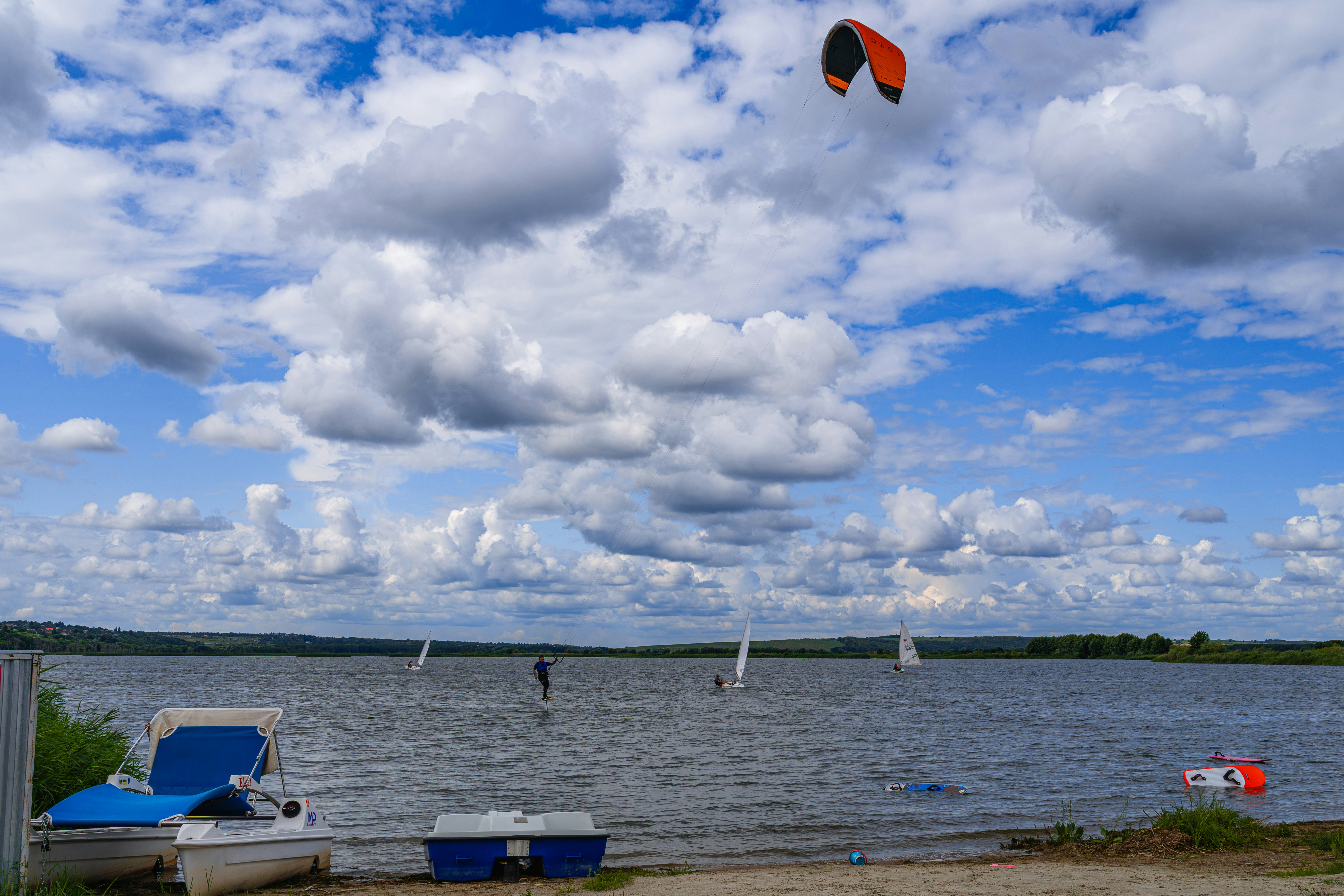 Seelandschaft mit Booten, Kitesurfern und einem wolkigen blauen Himmel.