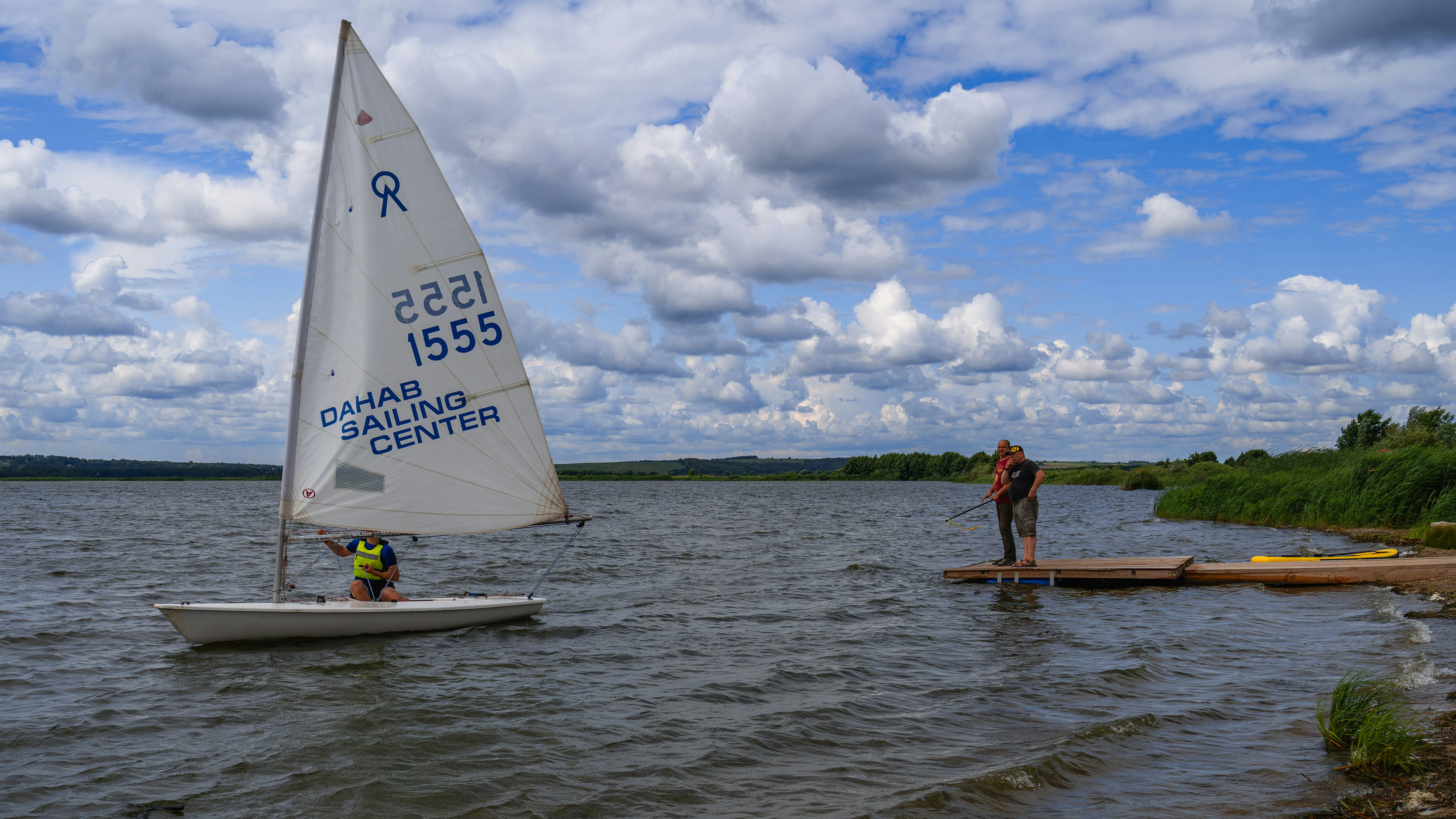 Segelboot auf einem See mit einer Person am Steg.