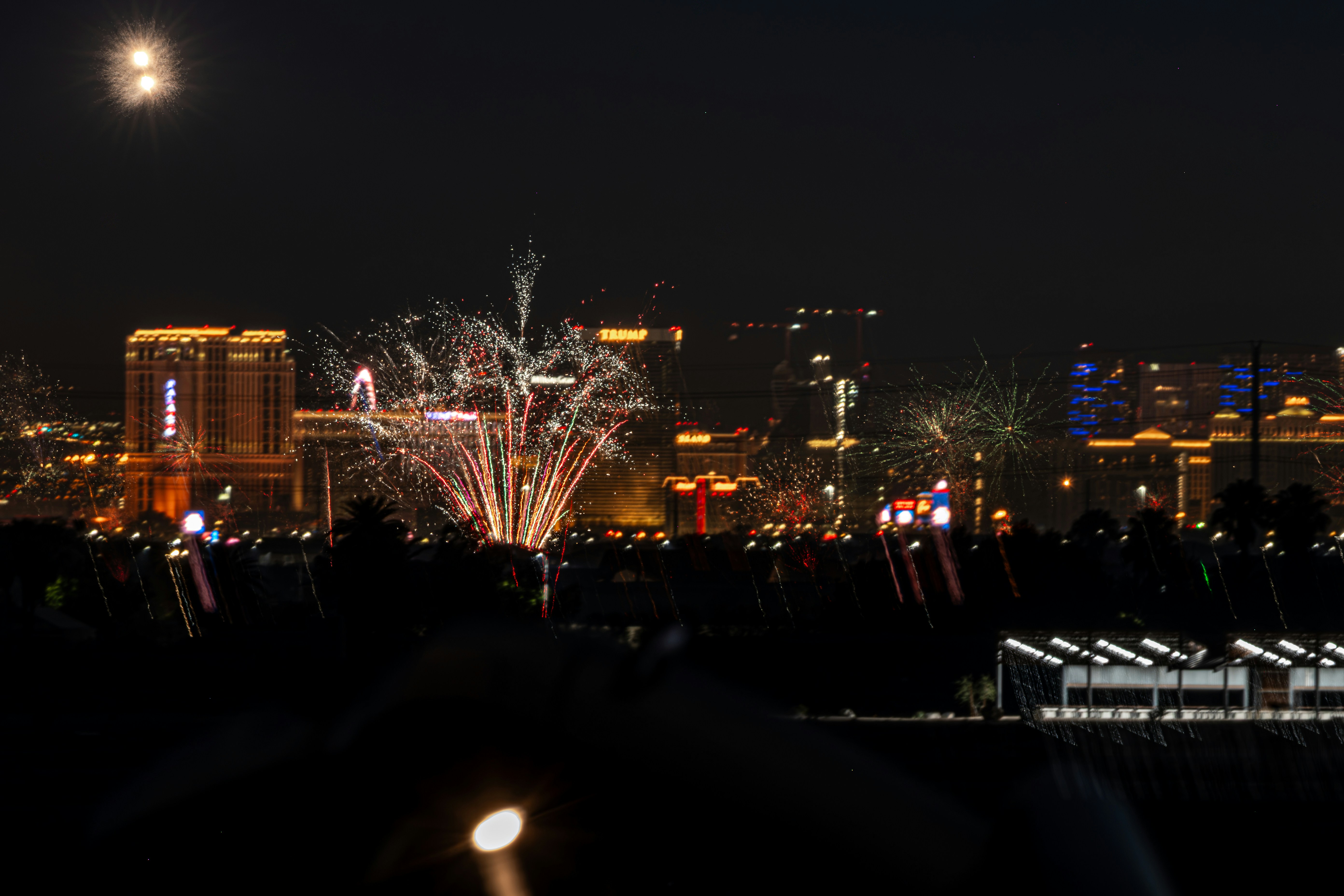 Des feux d’artifice illuminent le ciel nocturne au-dessus d’un paysage urbain lumineux.