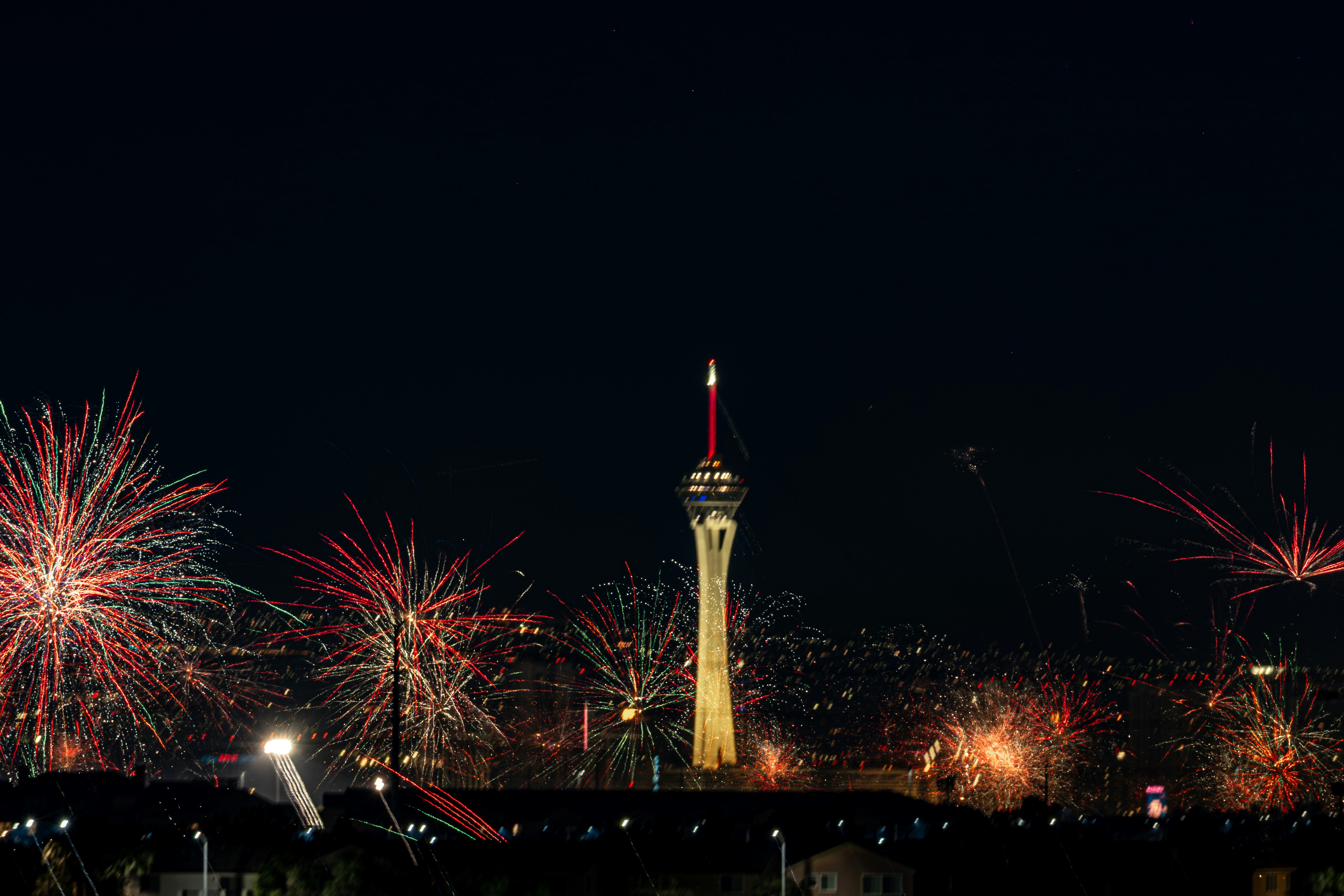 Des feux d’artifice colorés éclatent autour d’une haute tour la nuit.