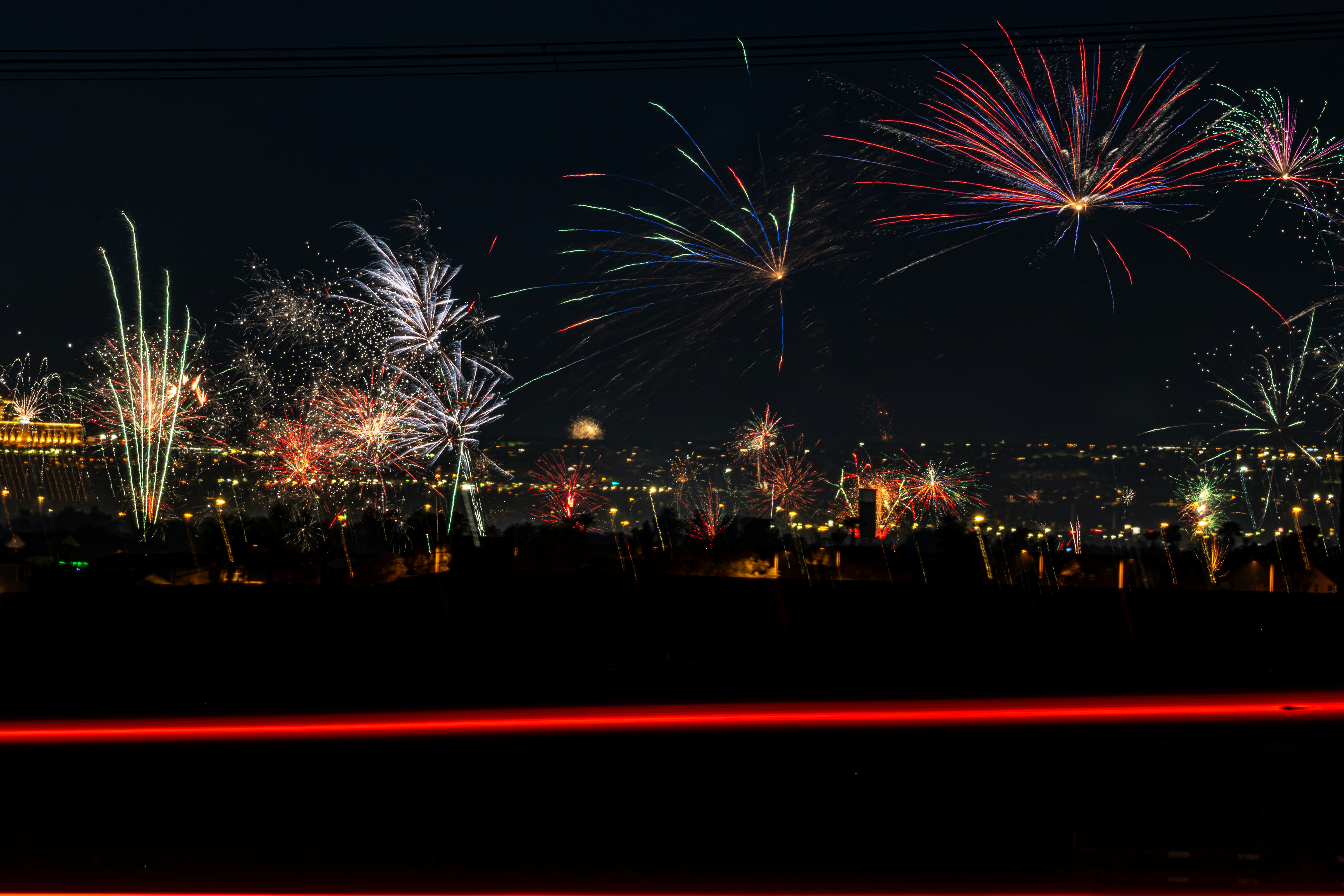 Des feux d’artifice éclatent sur la ligne d’horizon de la ville avec une traînée de lumière rouge bien visible.