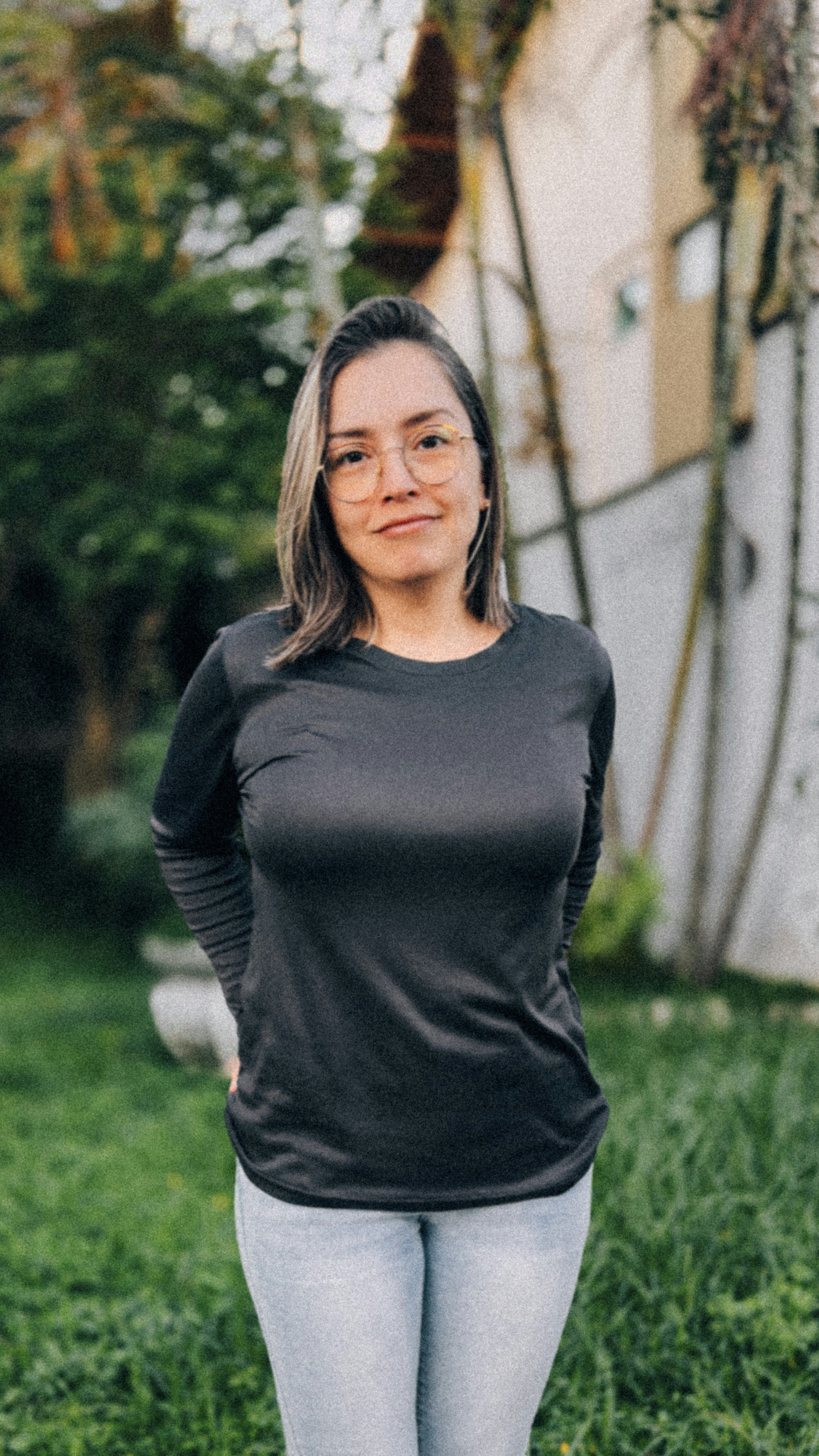 Joven con camisa negra y vaqueros sonriendo al aire libre.