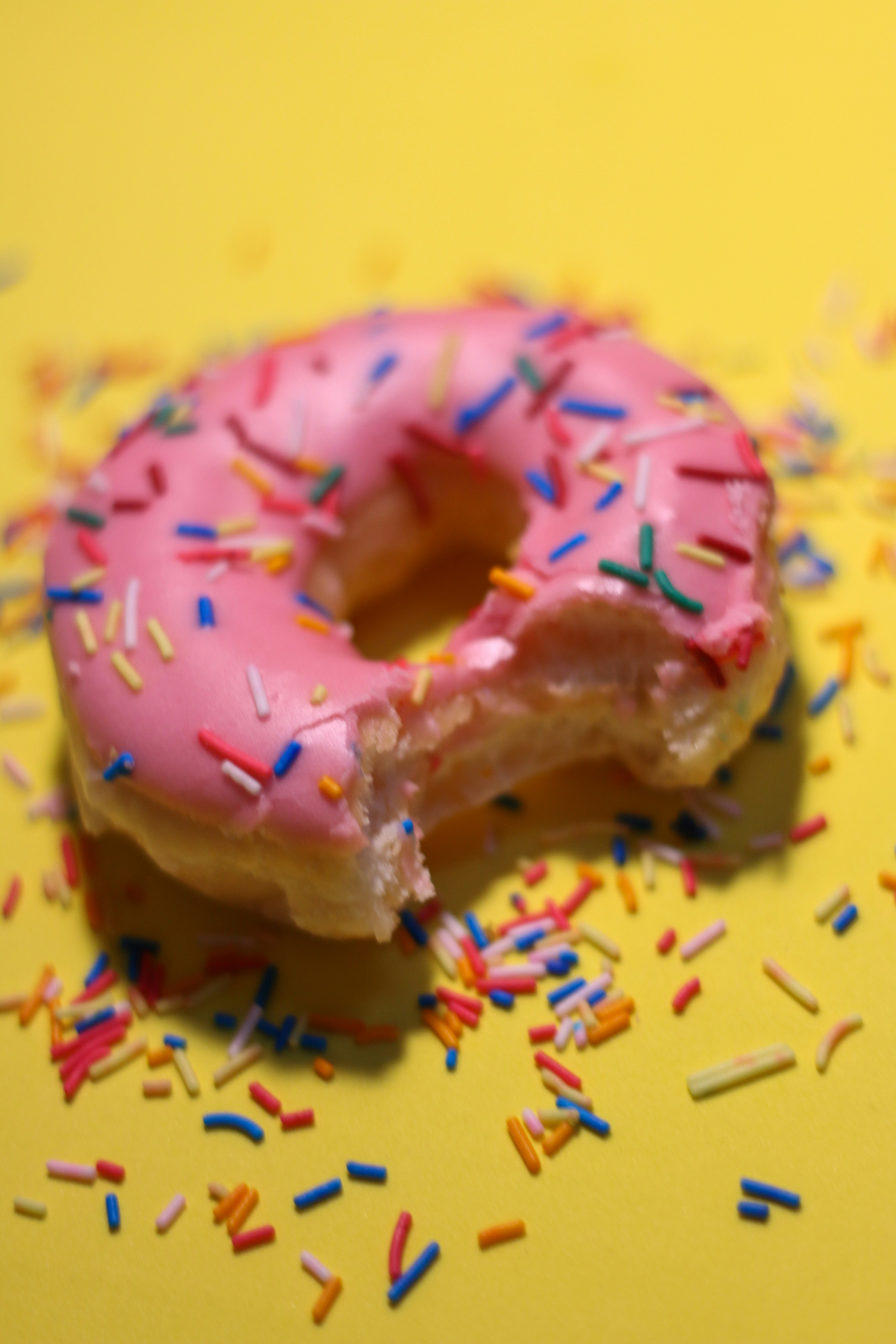 Bitten pink donut with colorful sprinkles on yellow background