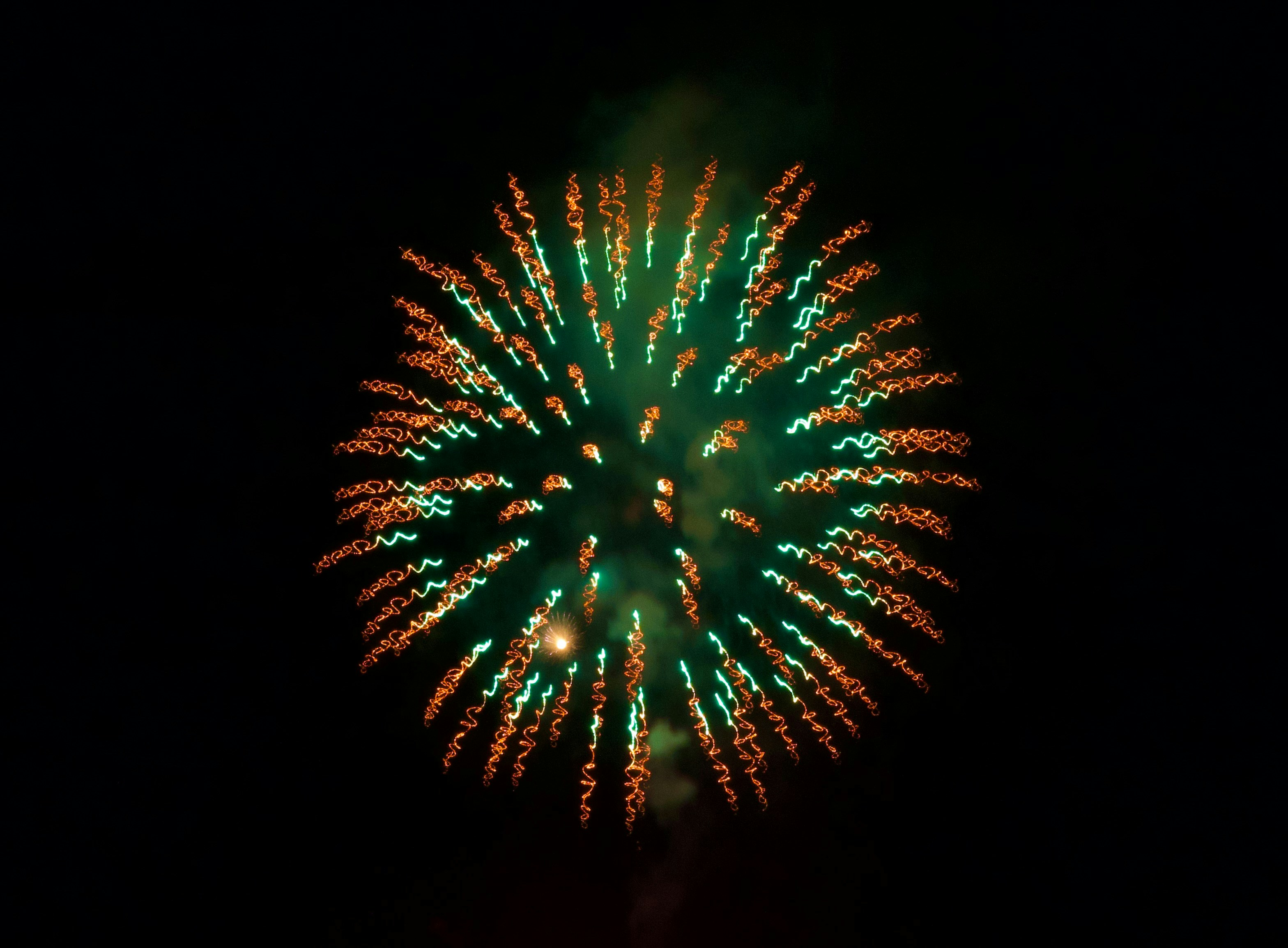 Un vivace fuoco d'artificio verde e arancione esplode nella notte.