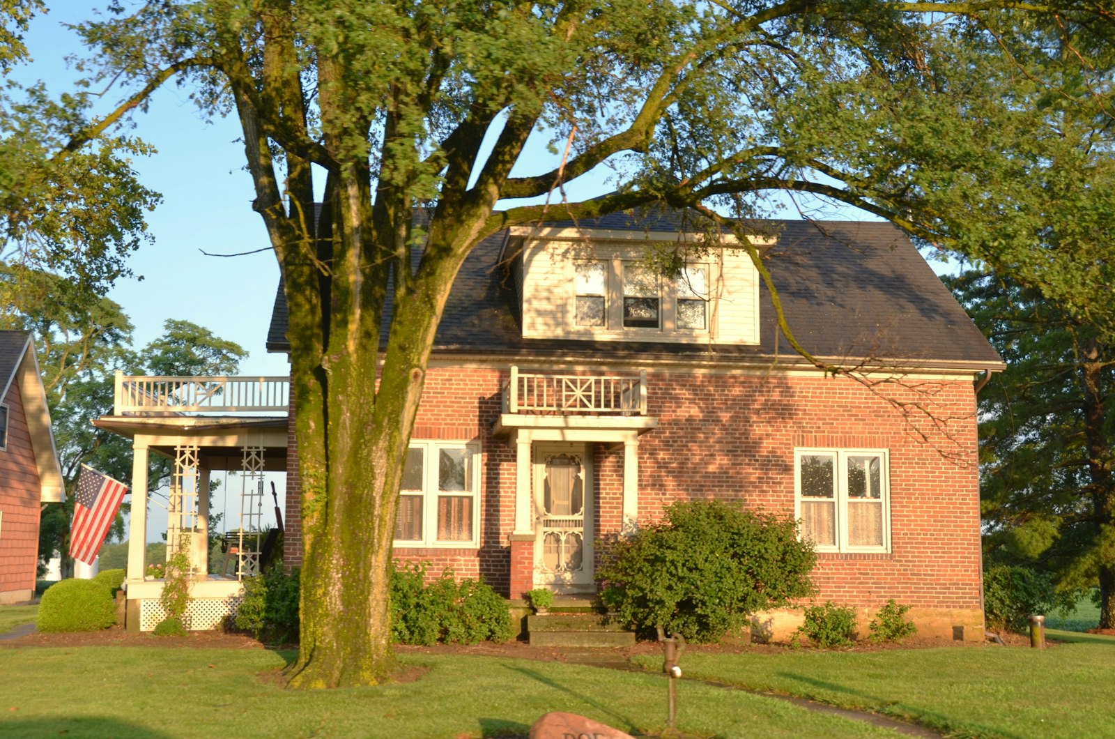 Older two story brick home in a wooded Milford OH neighborhood, white trim windows shaded by the mature tree canopy that coats east side glass with pollen and debris