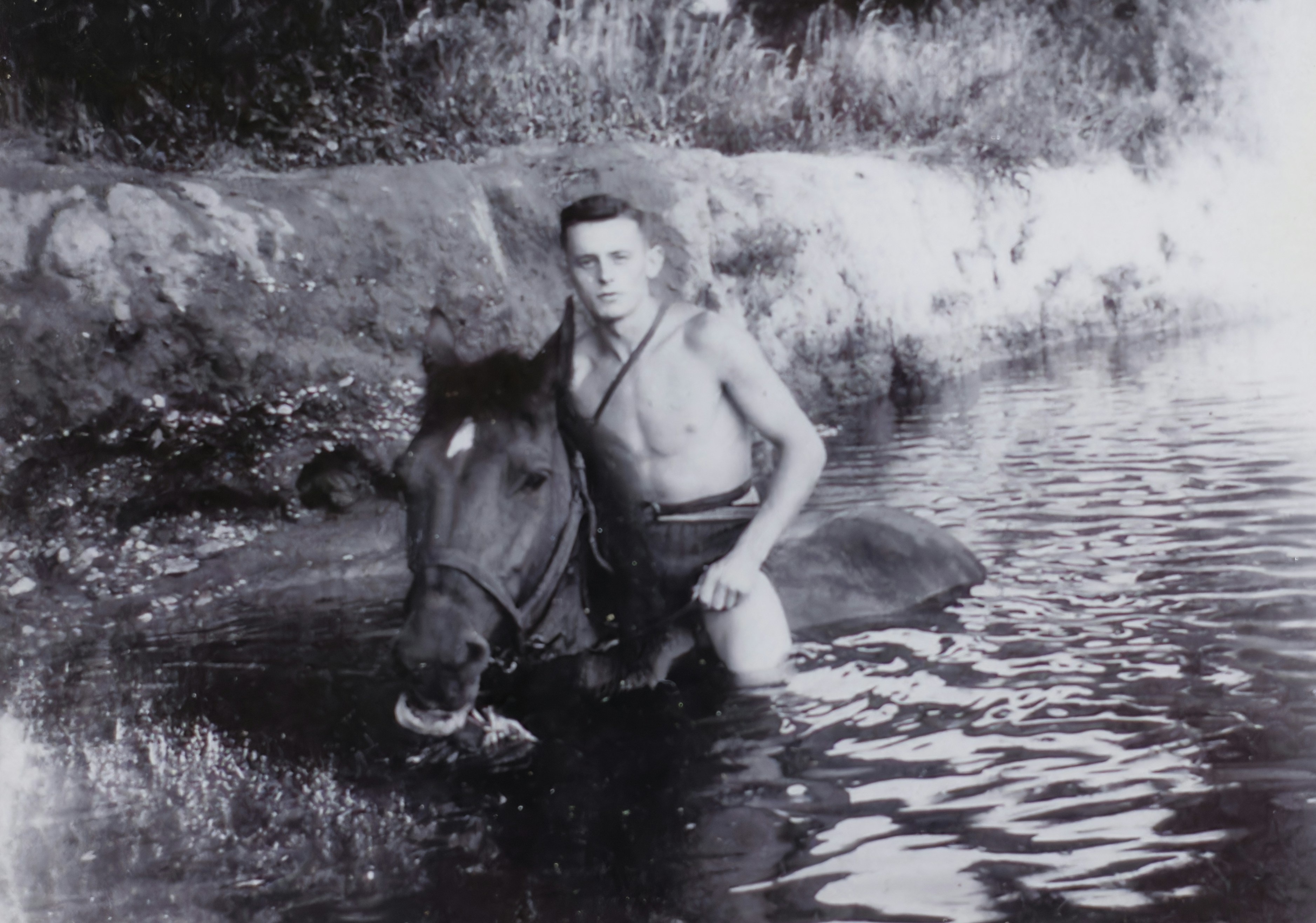 Man and horse wading in a shallow river.