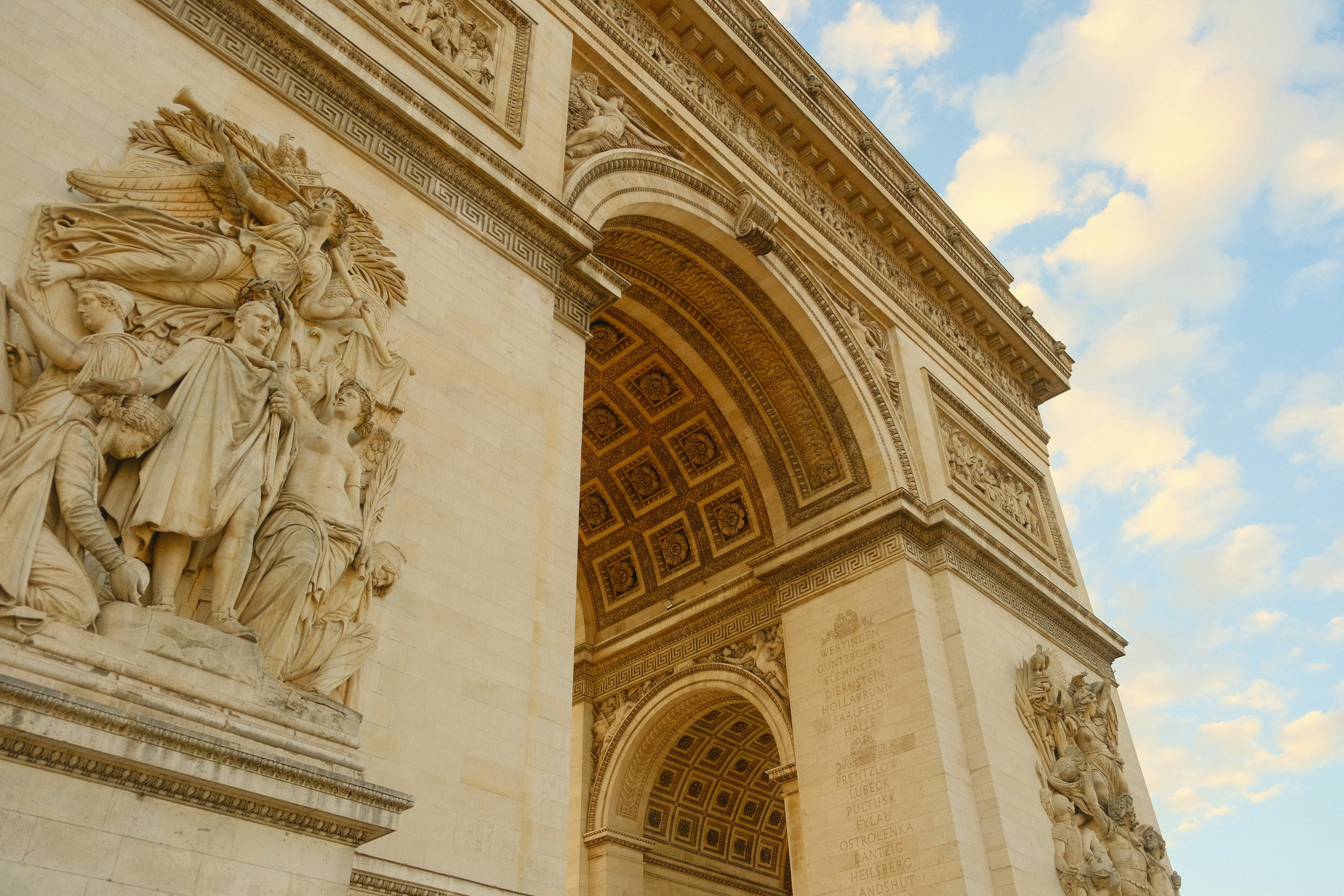 Ornate arc de triomphe architecture against a blue cloudy sky.