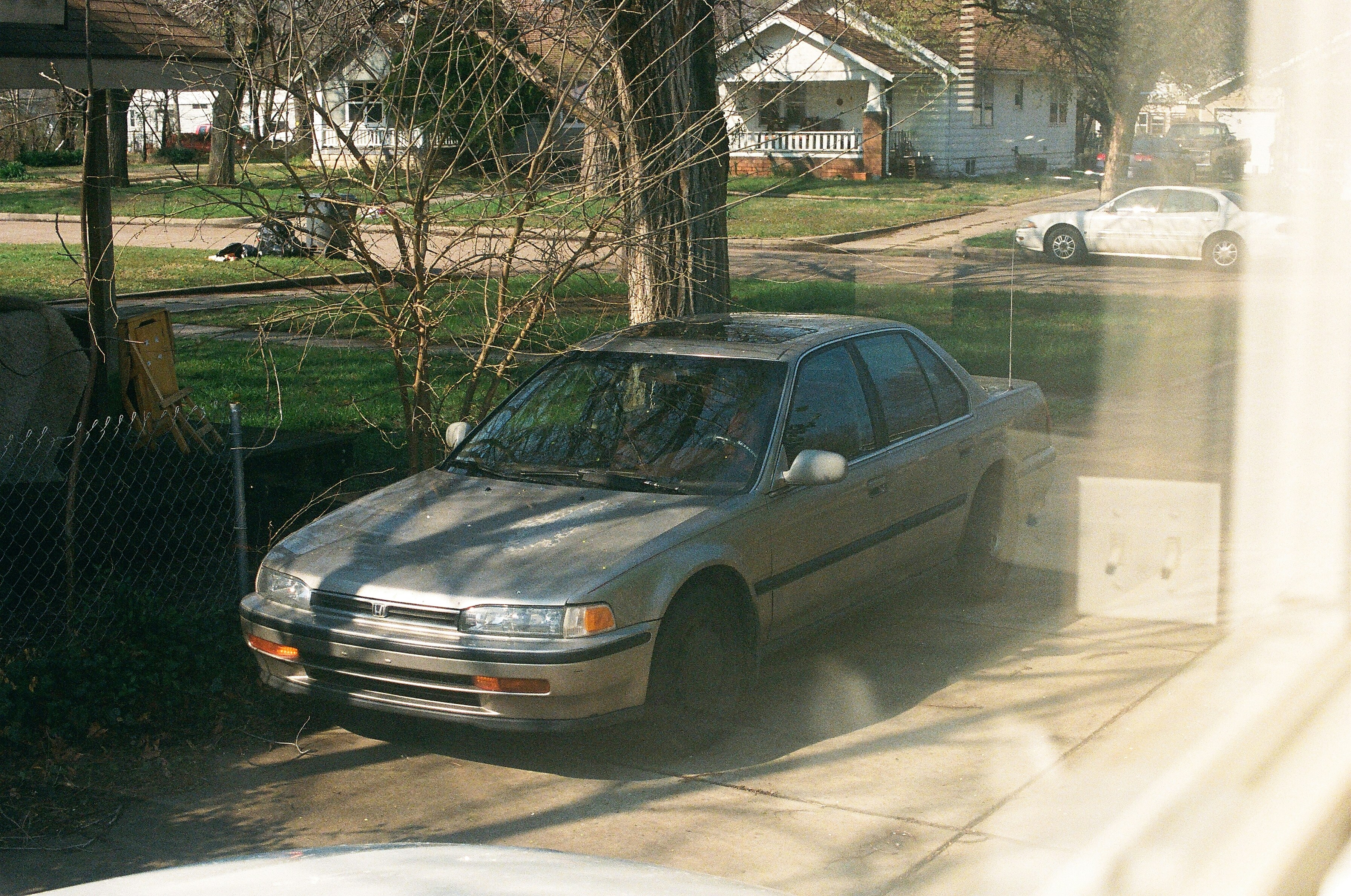 Gray sedan parked on a driveway in front of houses.