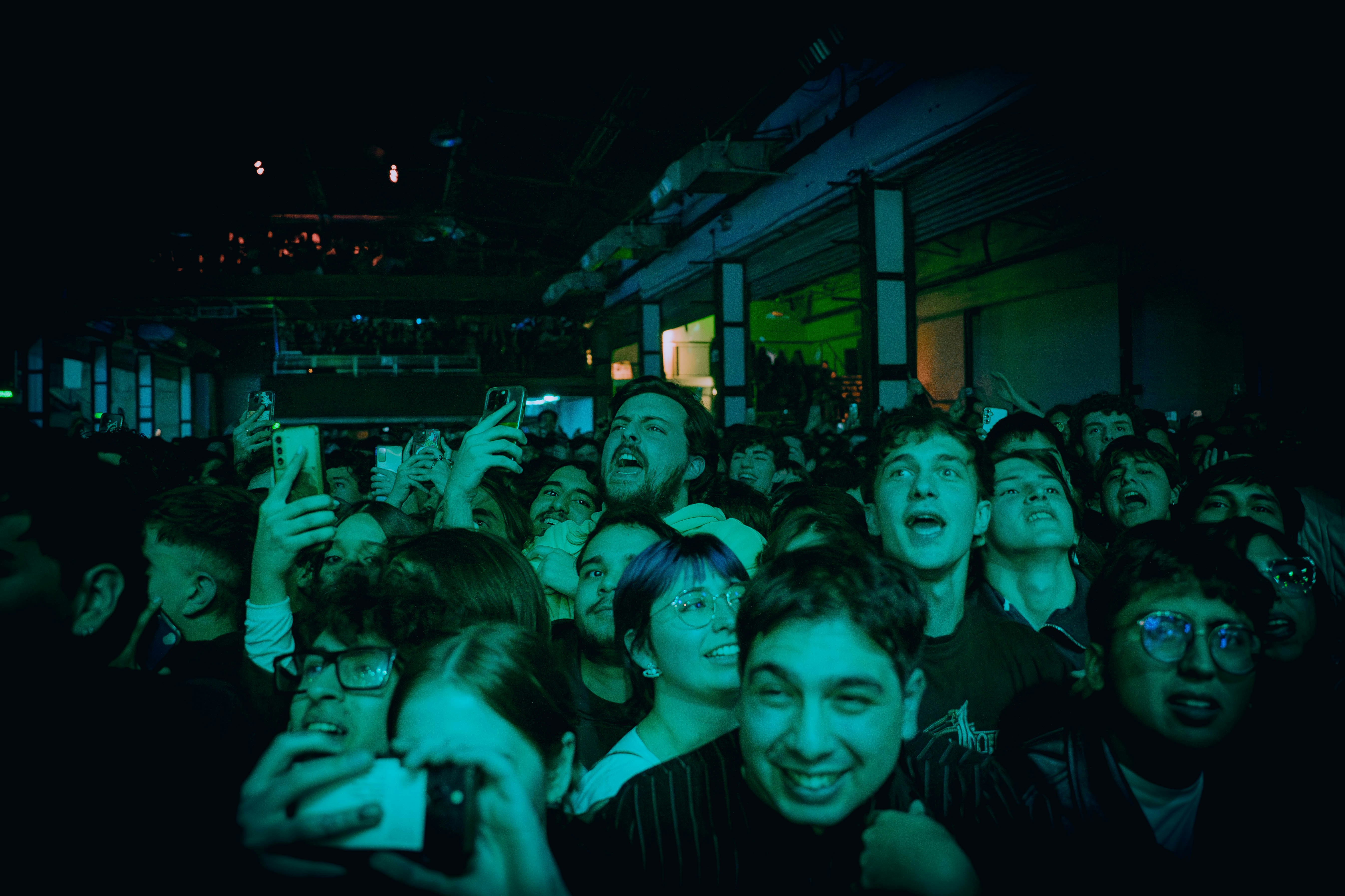 Excited crowd at a night concert with green lighting.