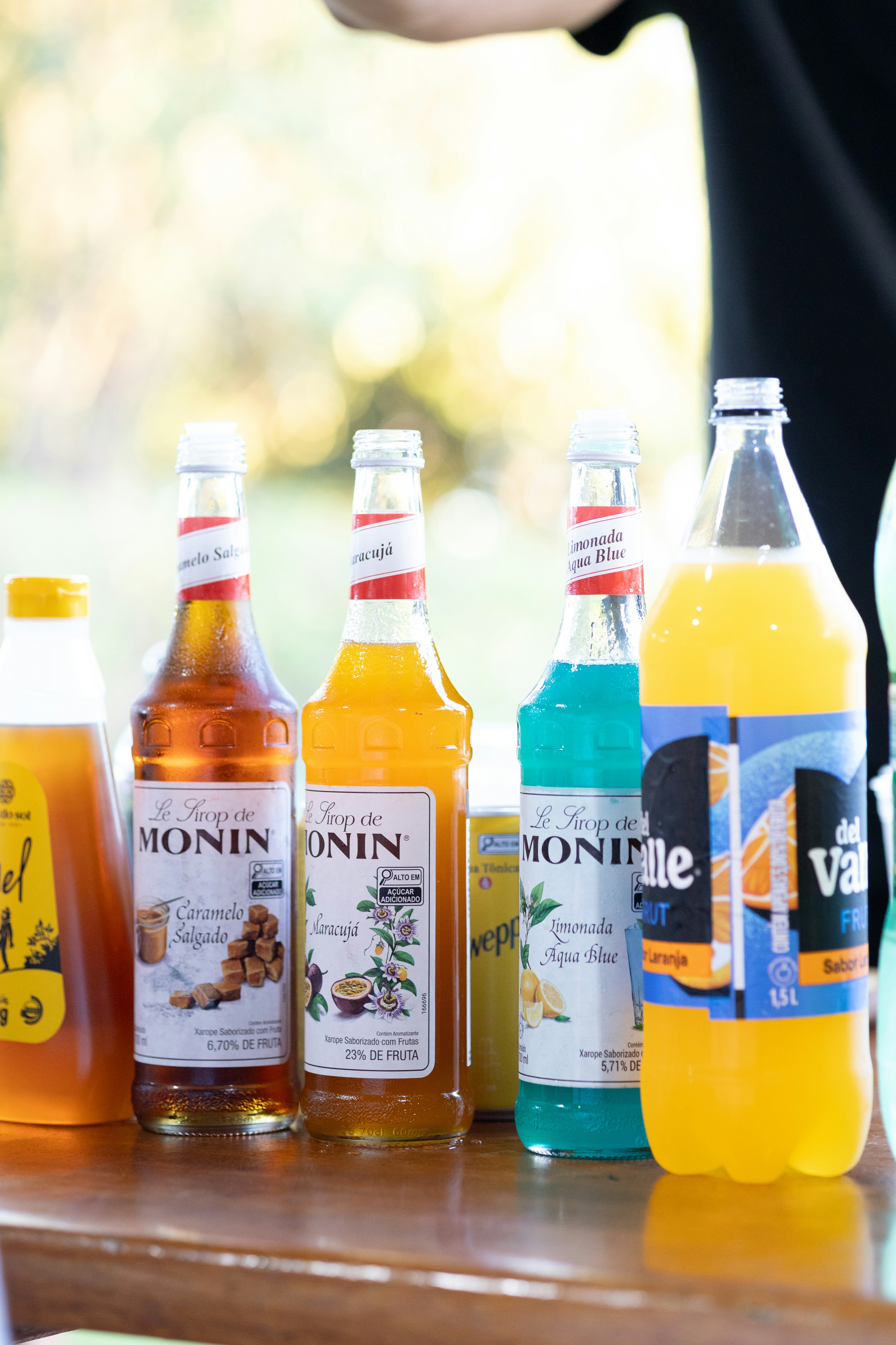 Assorted monin syrups and del valle orange soda bottles.