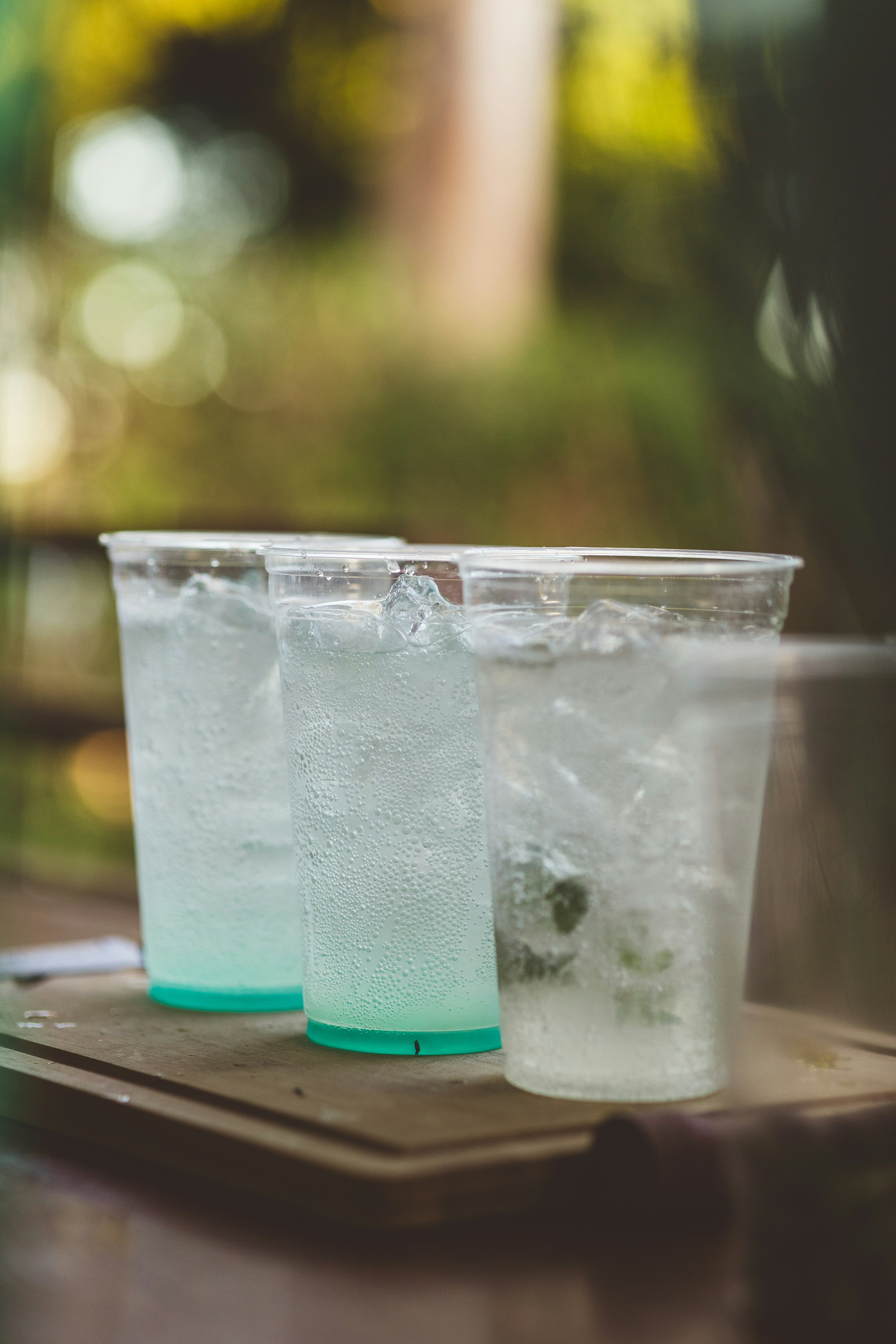 Three cold drinks with ice in plastic cups outdoors.
