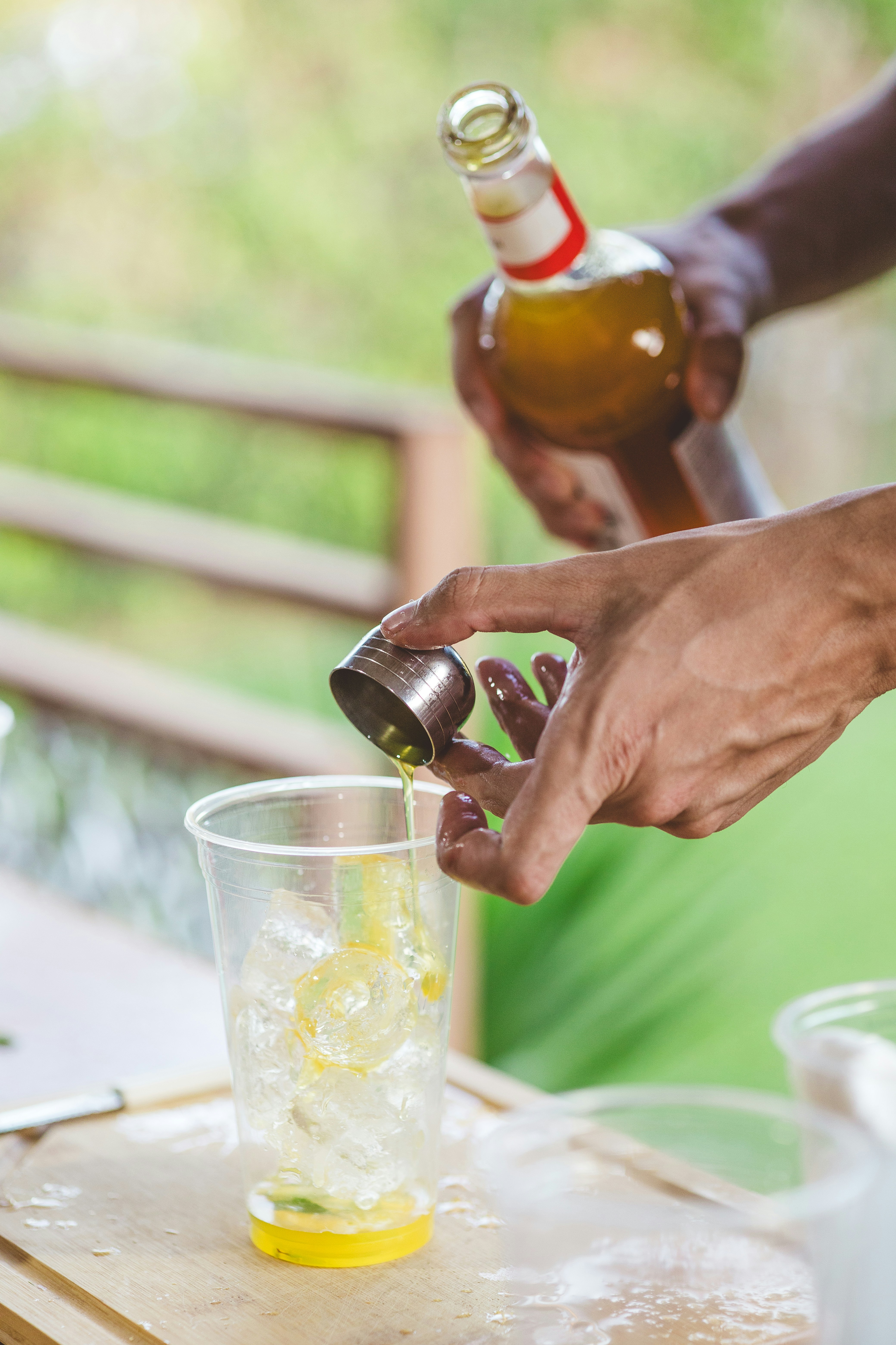 Hands pouring yellow liquid from a bottle into a cup.