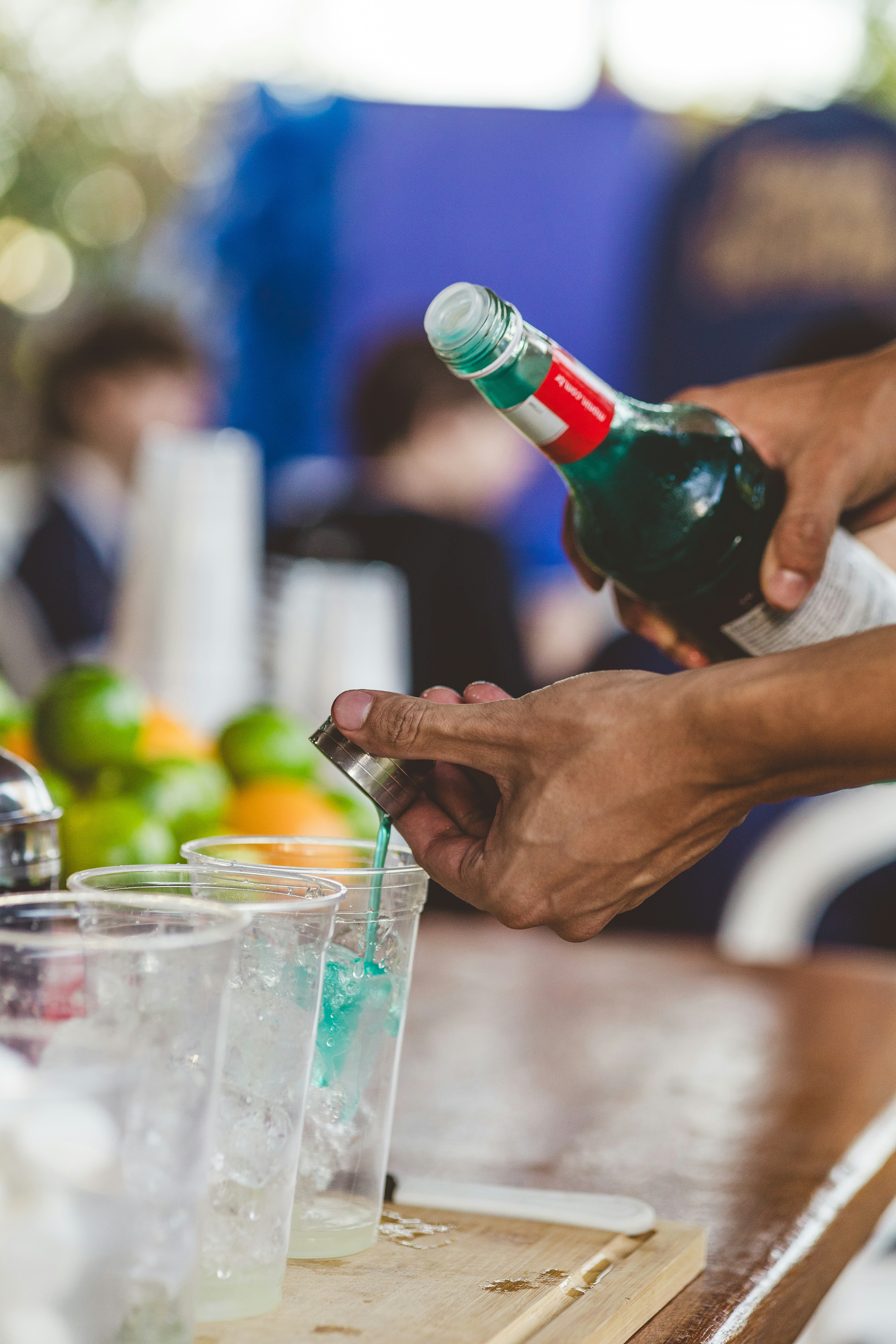 Hands pouring blue drink from bottle into plastic cup.