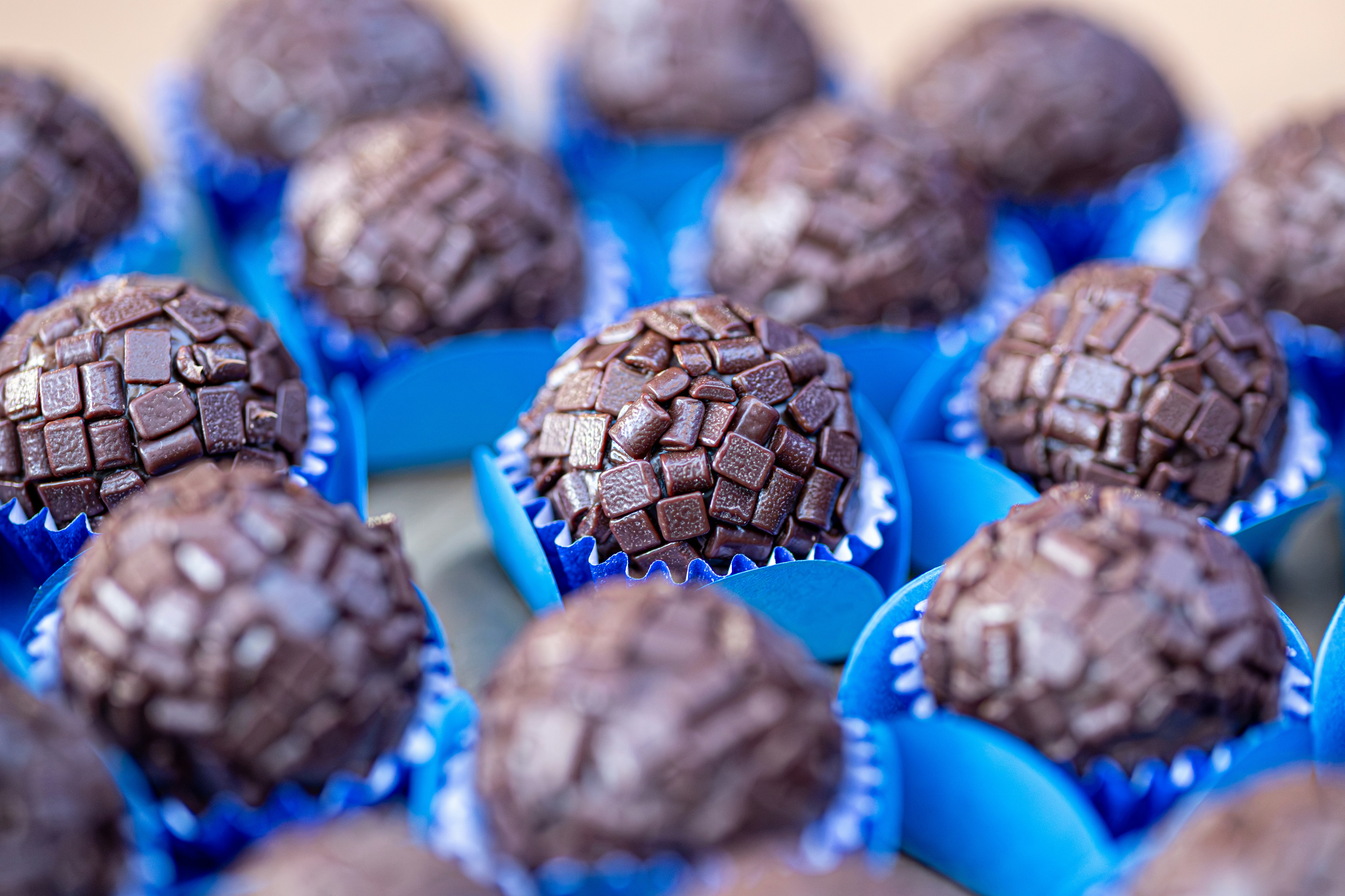 Many chocolate truffles with sprinkles in blue cups.